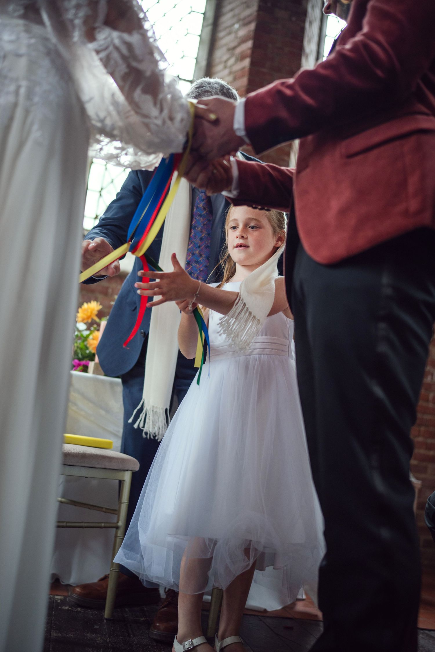 Young flower girl in white dress participates in colorful ribbon wedding ceremony ritual at red chapel Kells in Co Meath.