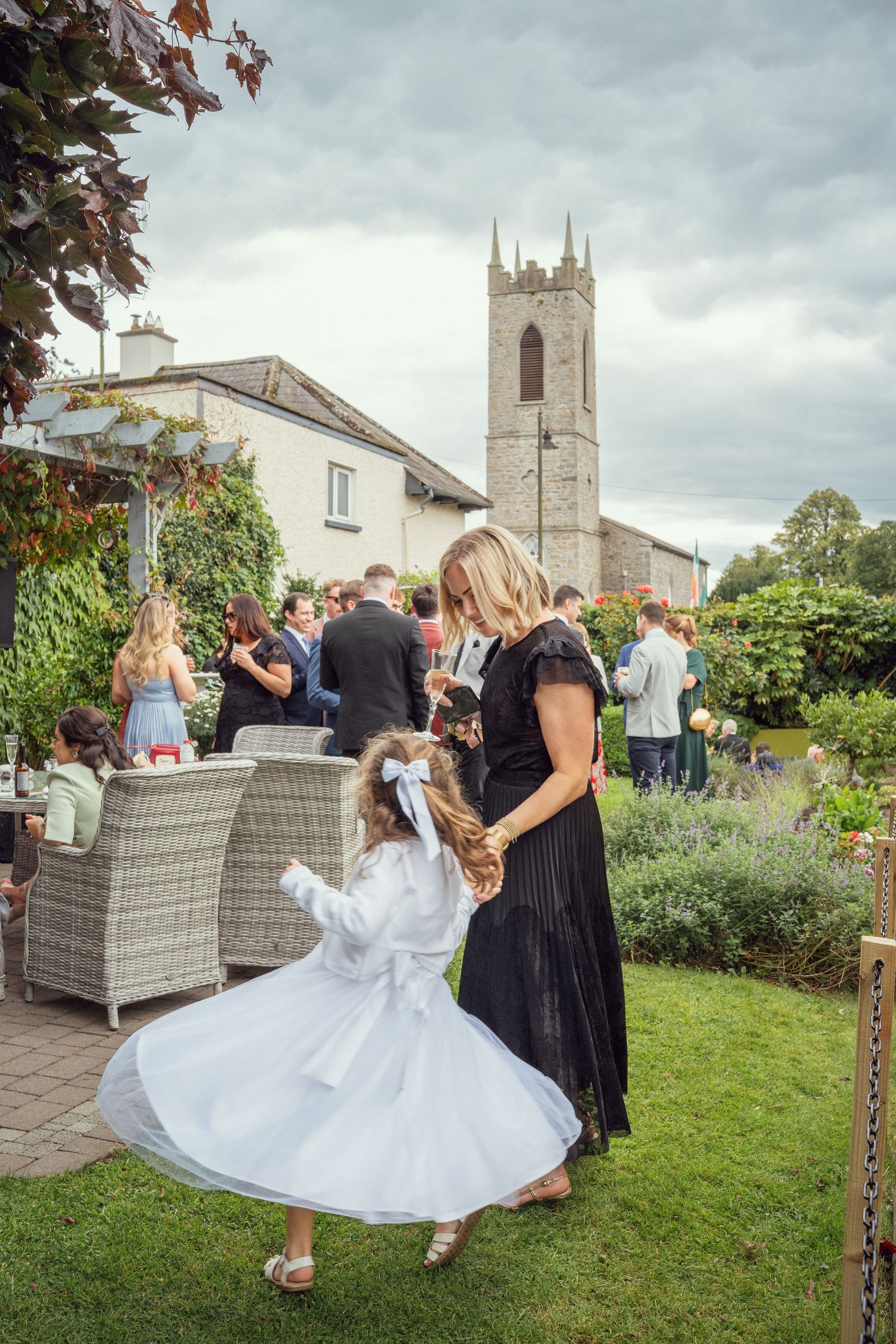 Mother twirls a flower girl in white dress at an outdoor wedding reception at outdoor garden wedding reception in Co Meath.