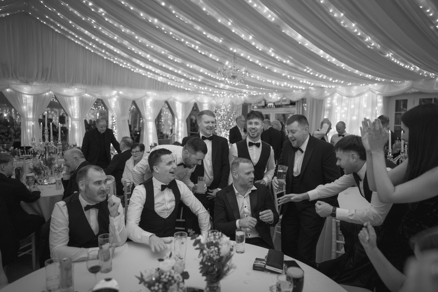 Guests laugh and celebrate together at a wedding reception inside a beautifully decorated fairy-lit marquee.