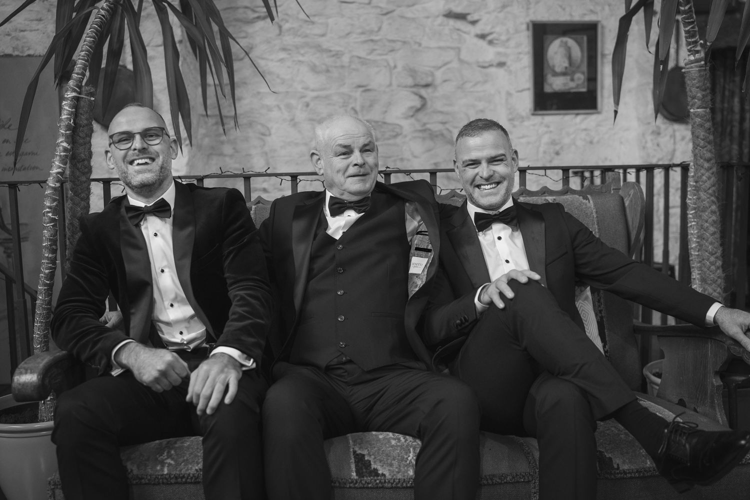 father and sons in tuxedos laughing together on a bench at the Manor House Mount Juliet wedding Kilkenny.