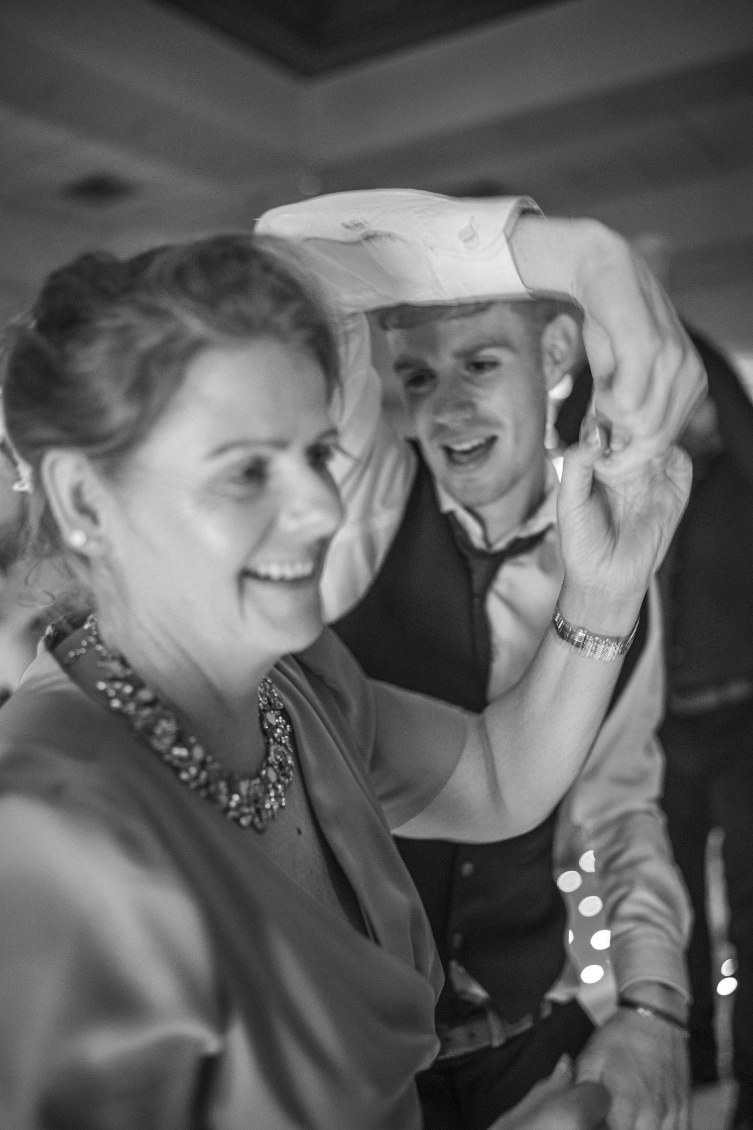 Joyful woman laughing as man places paper hat on her head during wedding reception dancing.