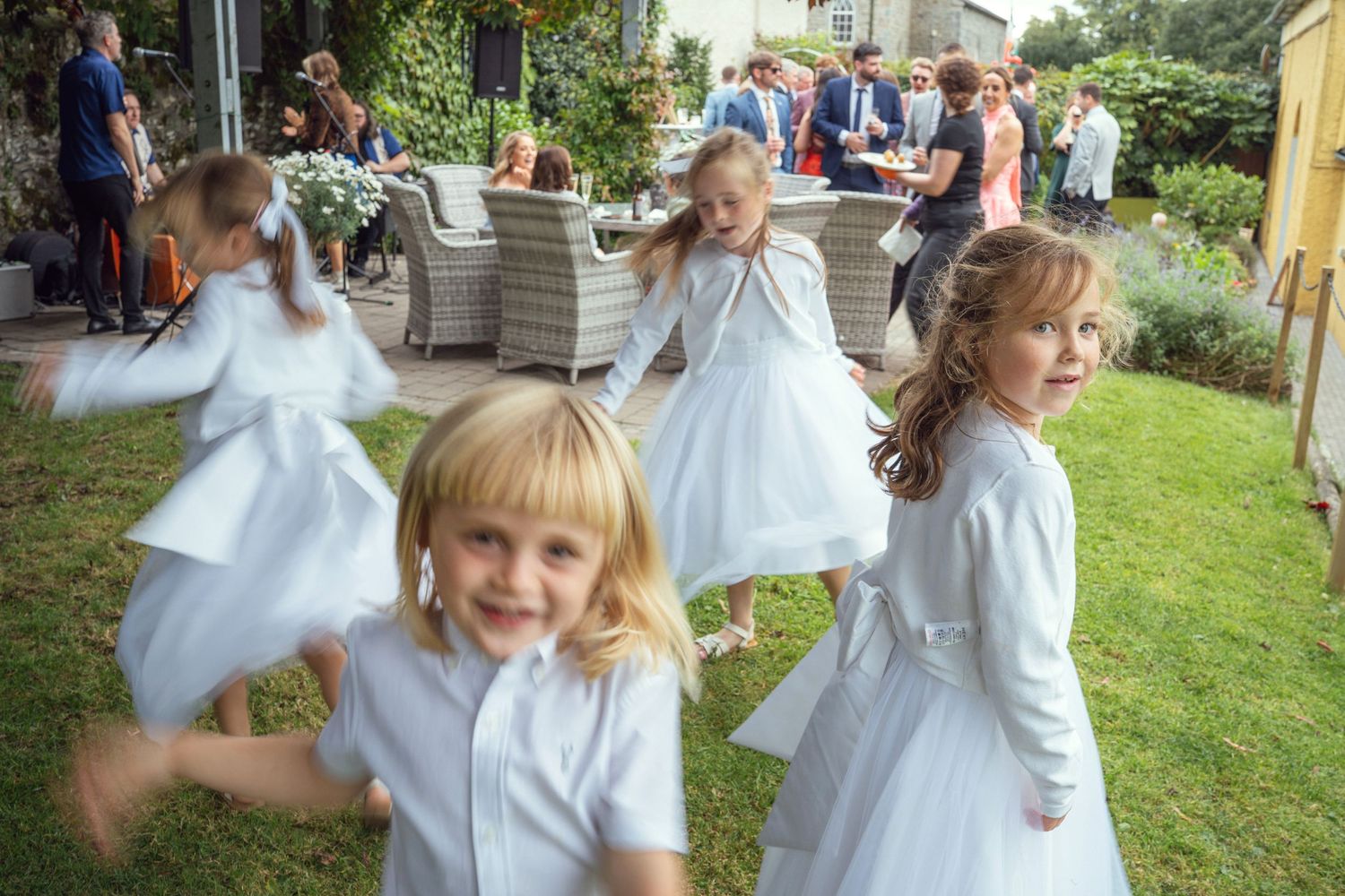 Flower girls in white dresses spinning and dancing joyfully on garden lawn outdoor garden wedding reception in Co Meath.
