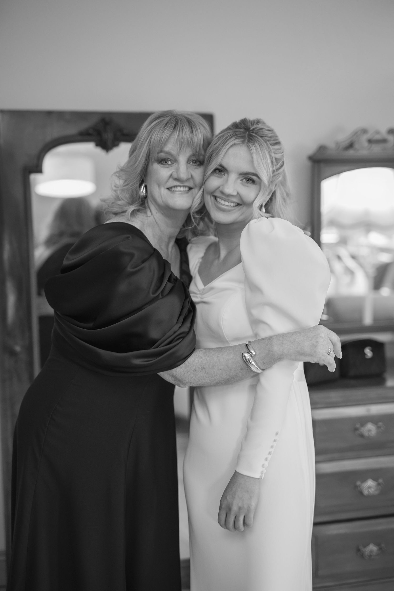 Bride and mother share a warm embrace in black and white wedding preparation photo.