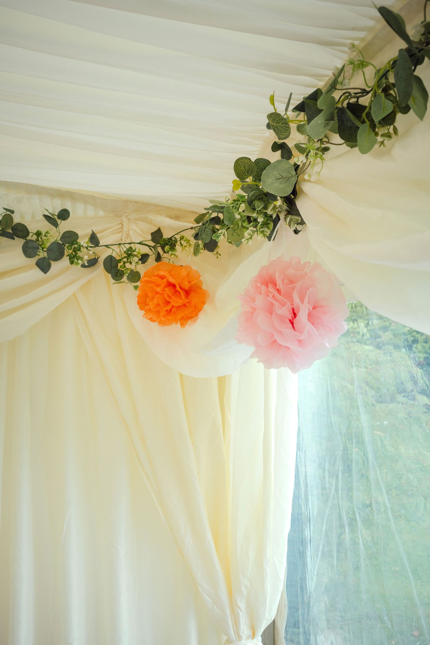 Wedding marquee ceiling decorated with eucalyptus garland and orange and pink tissue pom poms.