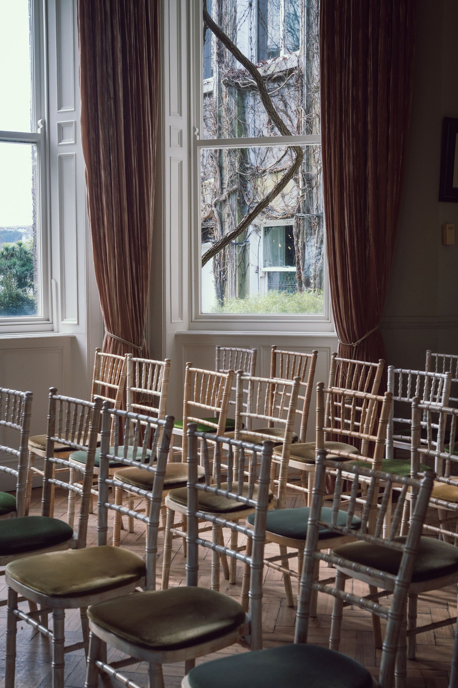 Rows of elegant chiavari chairs with green cushions set up for a wedding ceremony.