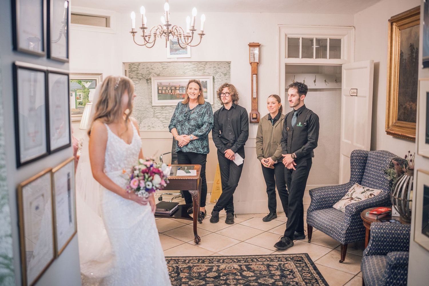 Bride in white lace gown shows her look to smiling guests in an elegant room before the wedding ceremony.