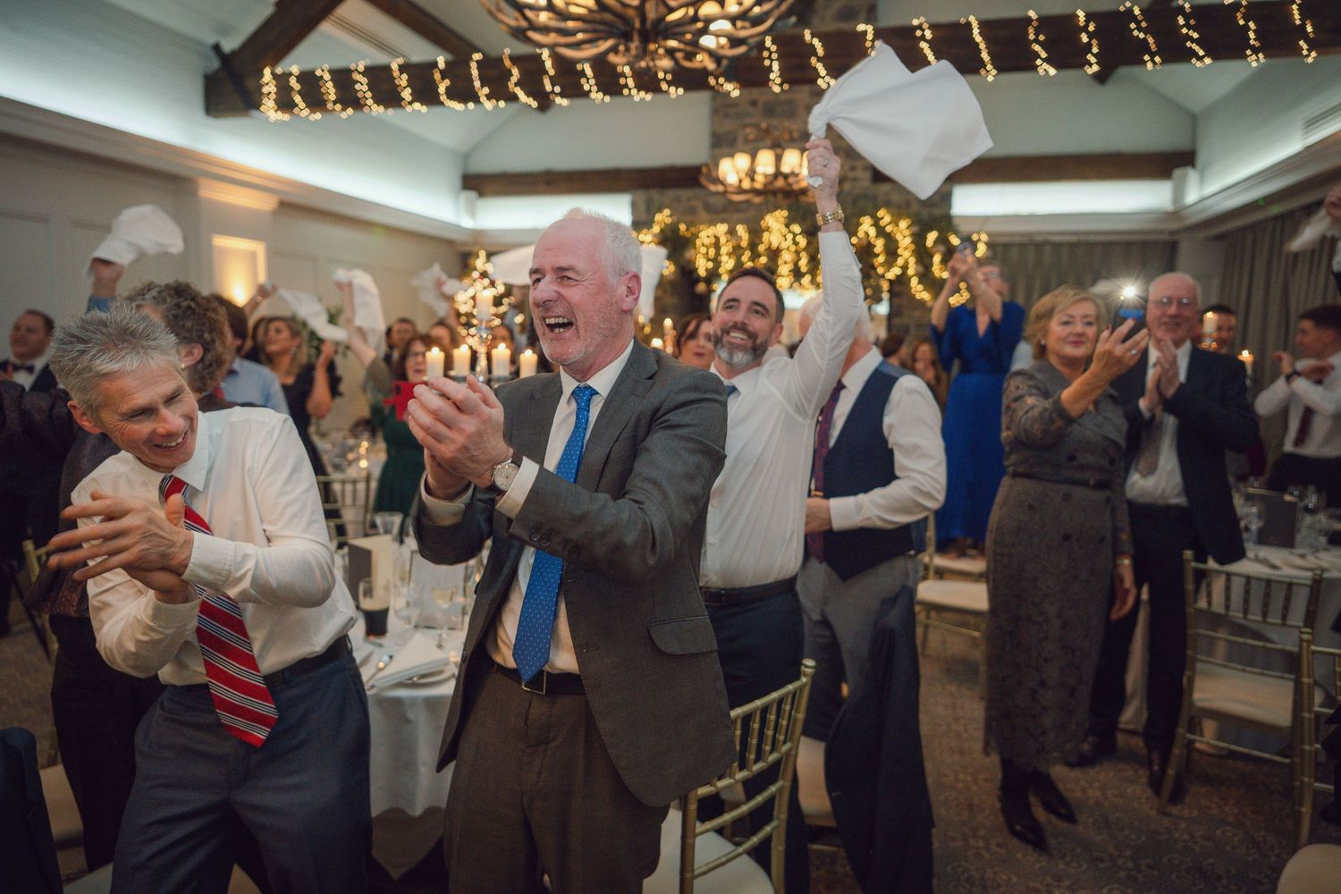 Excited wedding guests clapping and waving napkins in celebration during the reception dinner at Mount Juliet wedding in Kilkenny.