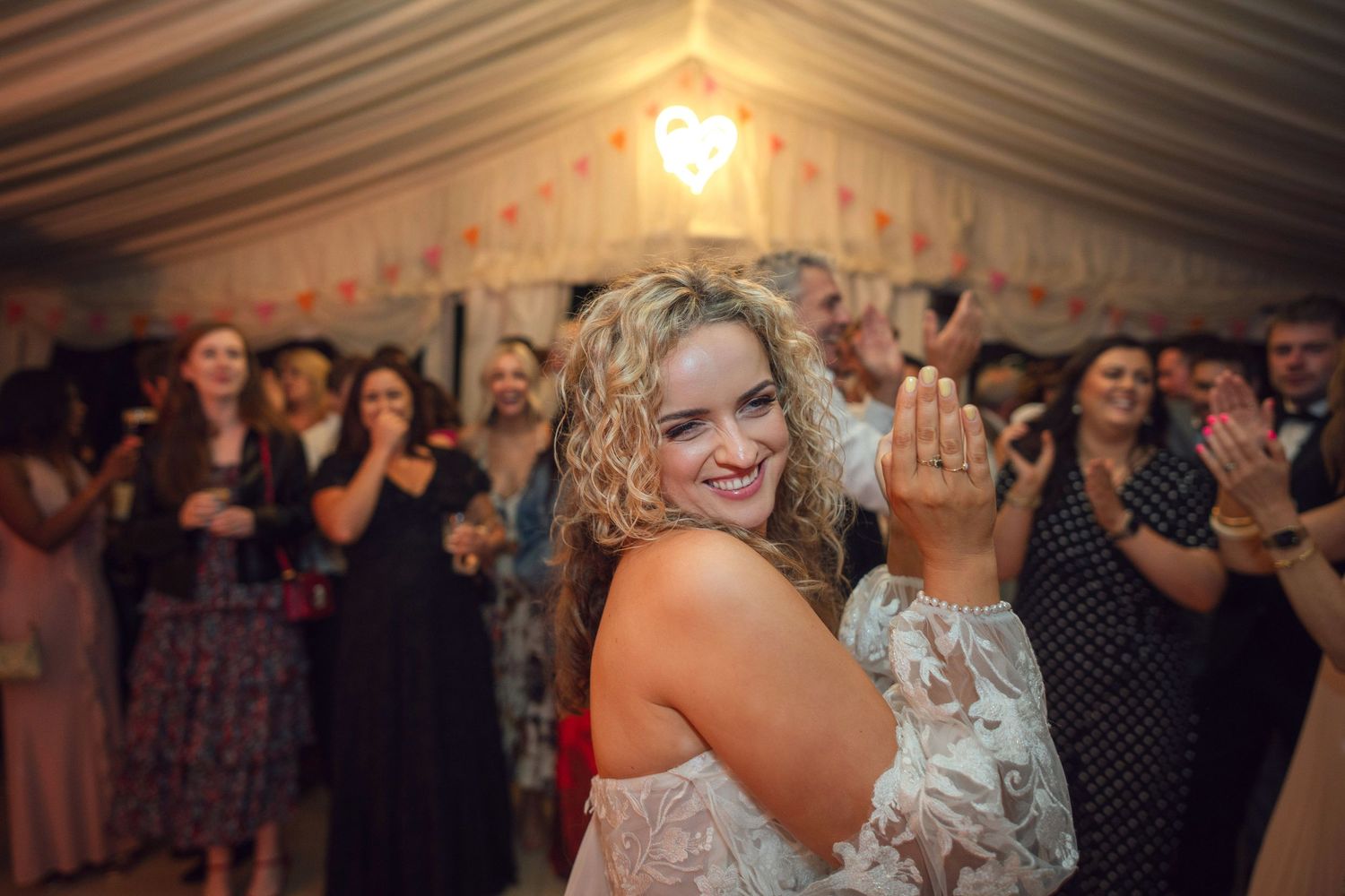 Bride claps on the dance floor at her wedding reception in a marquee at outdoor garden wedding reception in Co Meath.