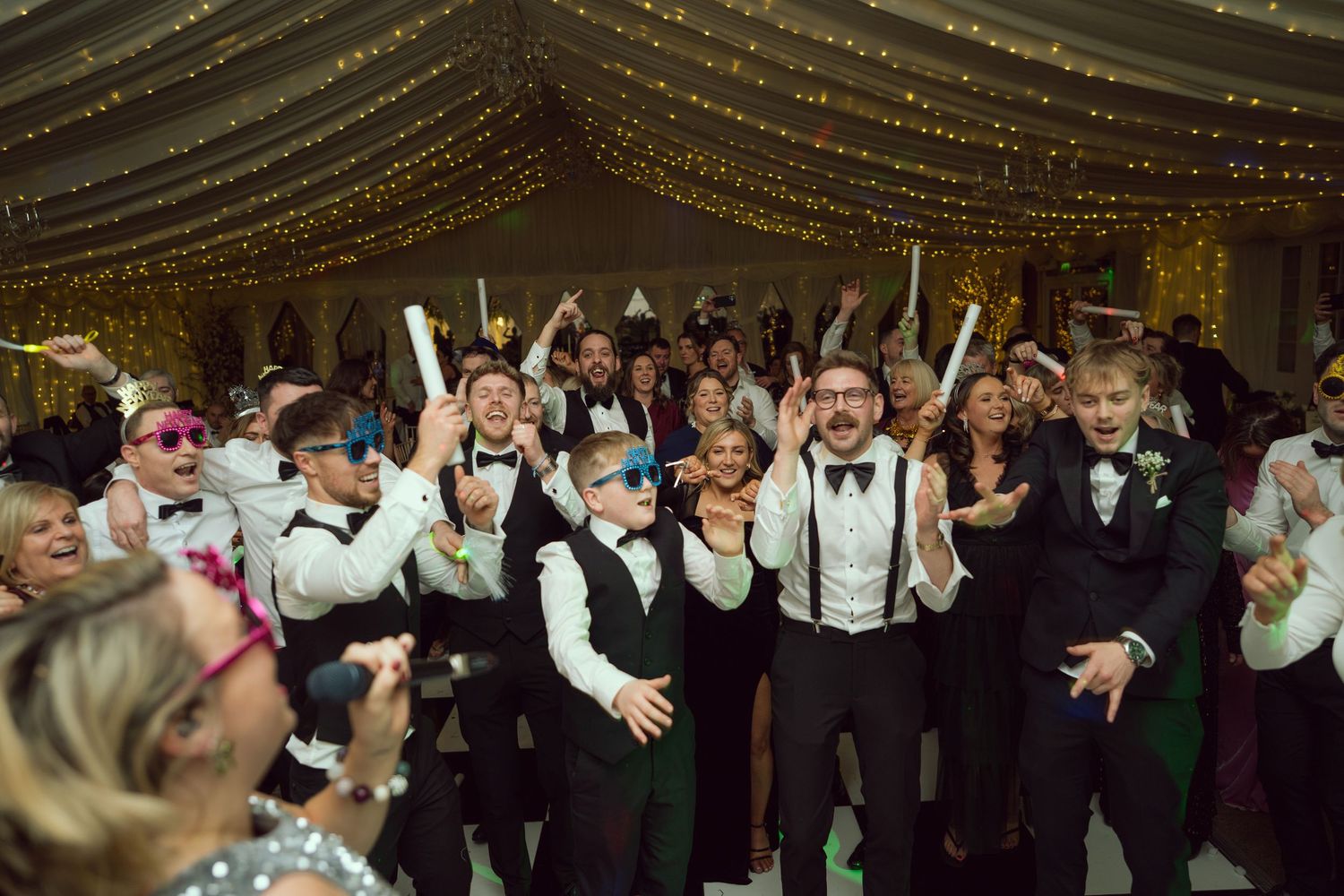 Energetic wedding reception dance floor filled with guests in formal attire celebrating joyfully.