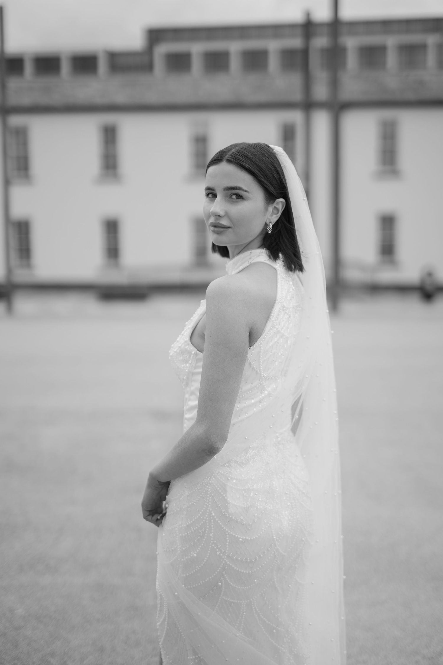 Bride in embellished halter wedding dress and veil poses outdoors in black and white photo.