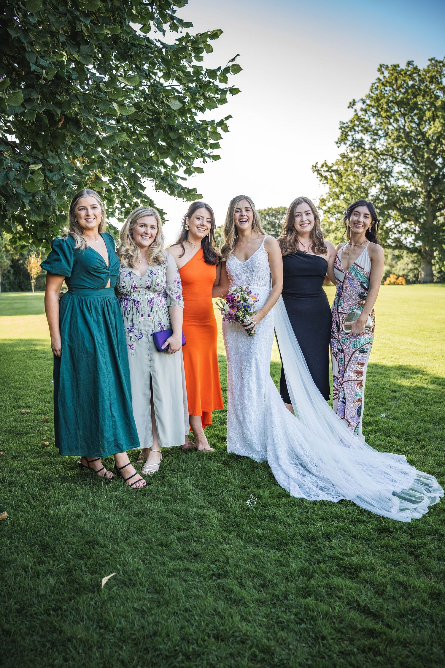 Bride in white lace gown poses with five female wedding guests outdoors at Rathsallagh House wedding in Wicklow.