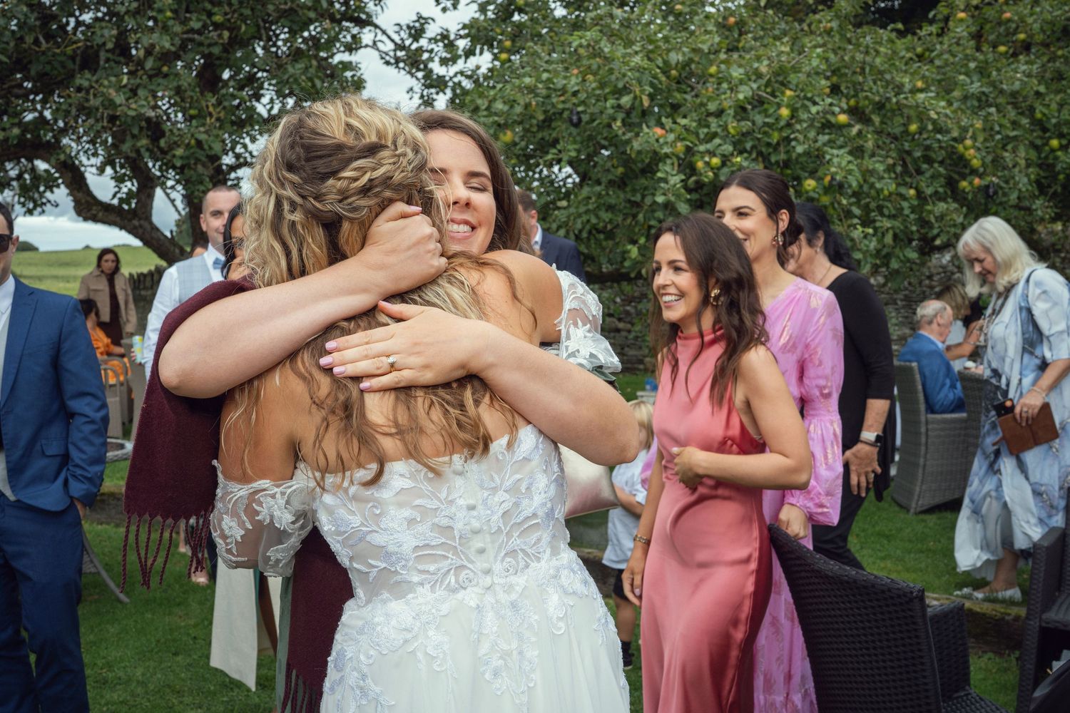 Bride in lace wedding gown shares warm embrace with guest during joyful outdoor at outdoor garden wedding reception in Co Meath.