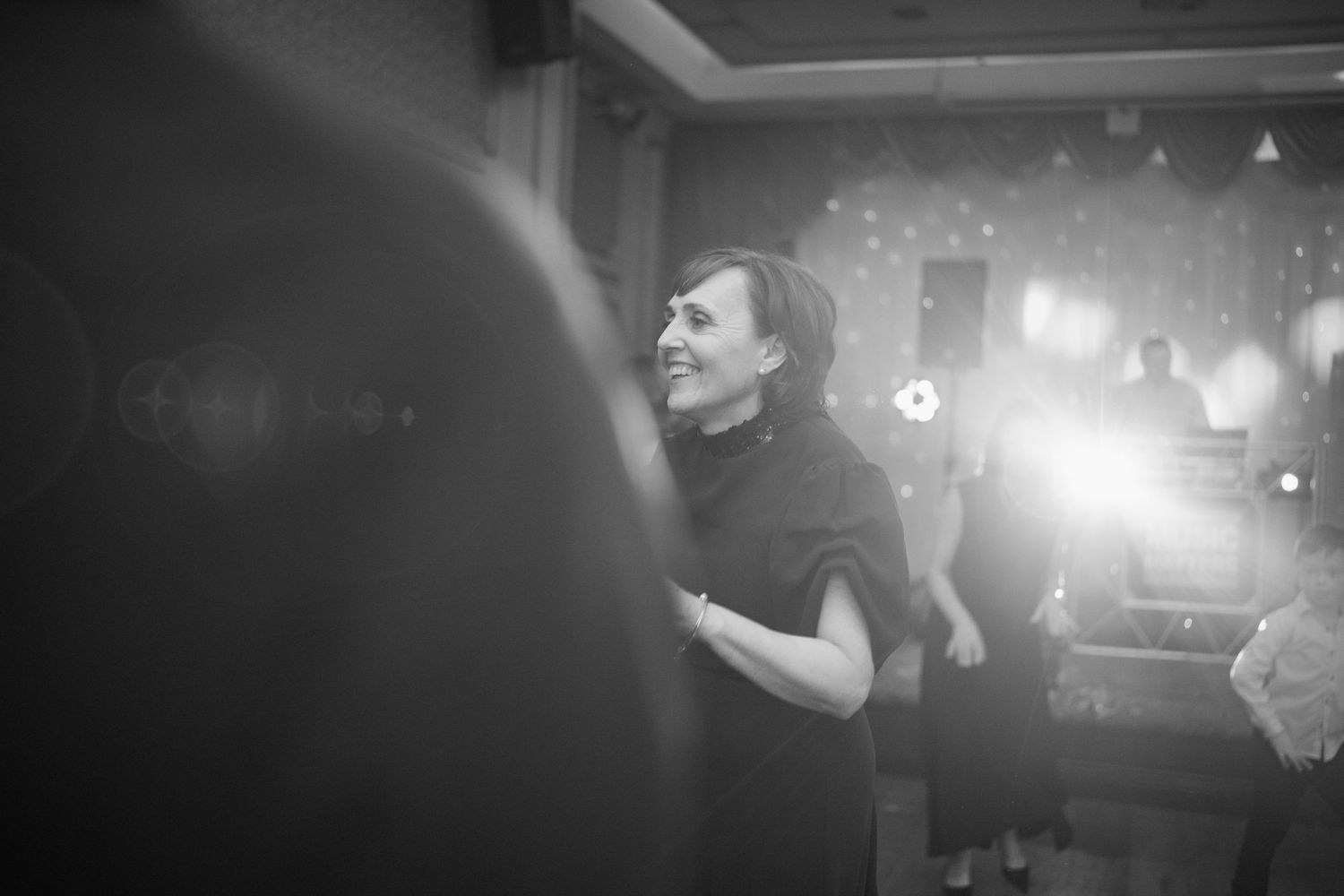 Black and white candid photo of a smiling woman in a black dress enjoying a wedding reception celebration.