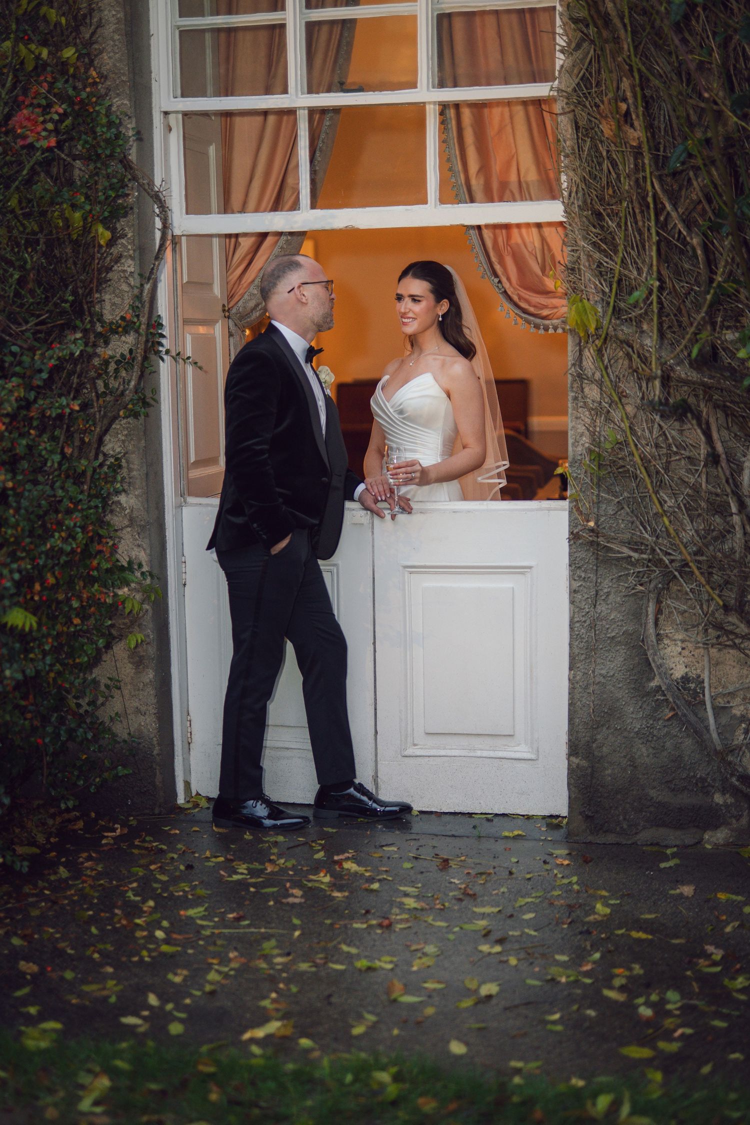 Bride in white gown and older gentleman in black suit standing in an elegant doorway at a wedding venue.