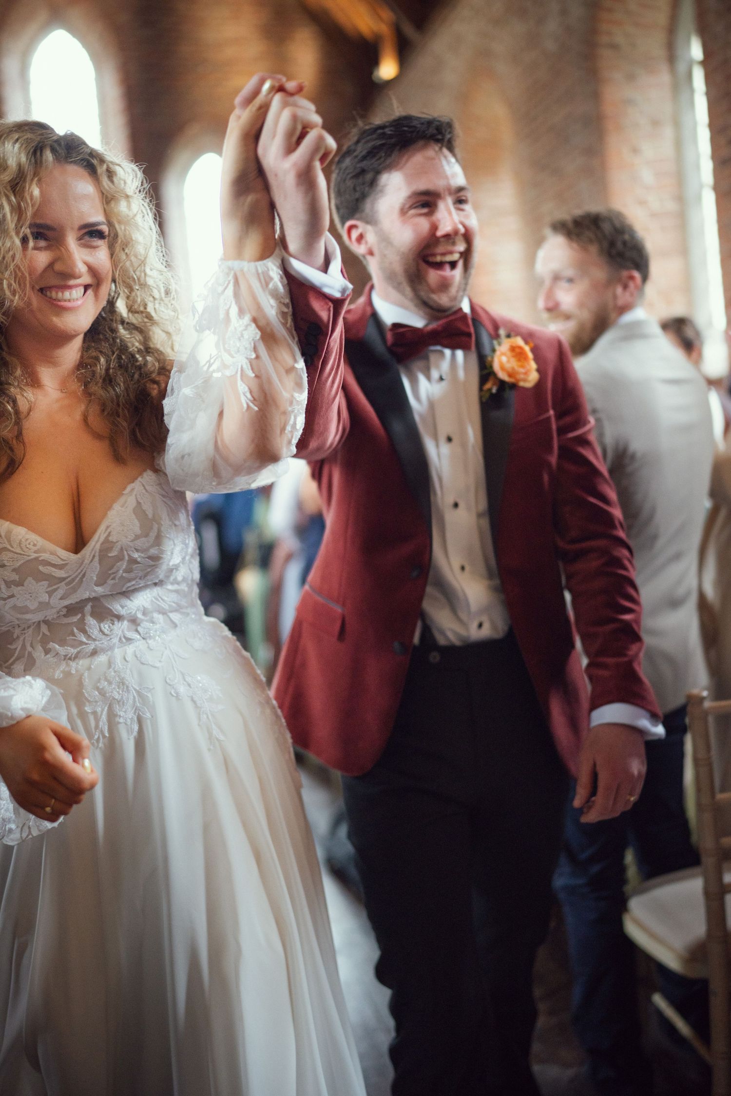 Smiling newlyweds raise hands in celebration while walking down church aisle at red chapel Kells in Co Meath.
