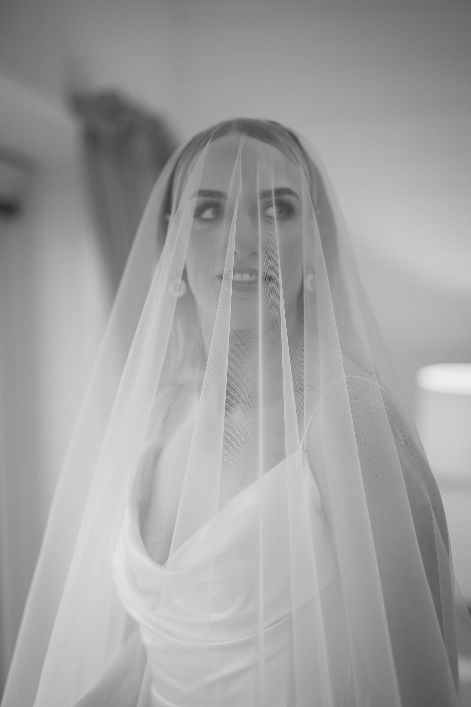 Black and white bridal portrait with veil draped over face.