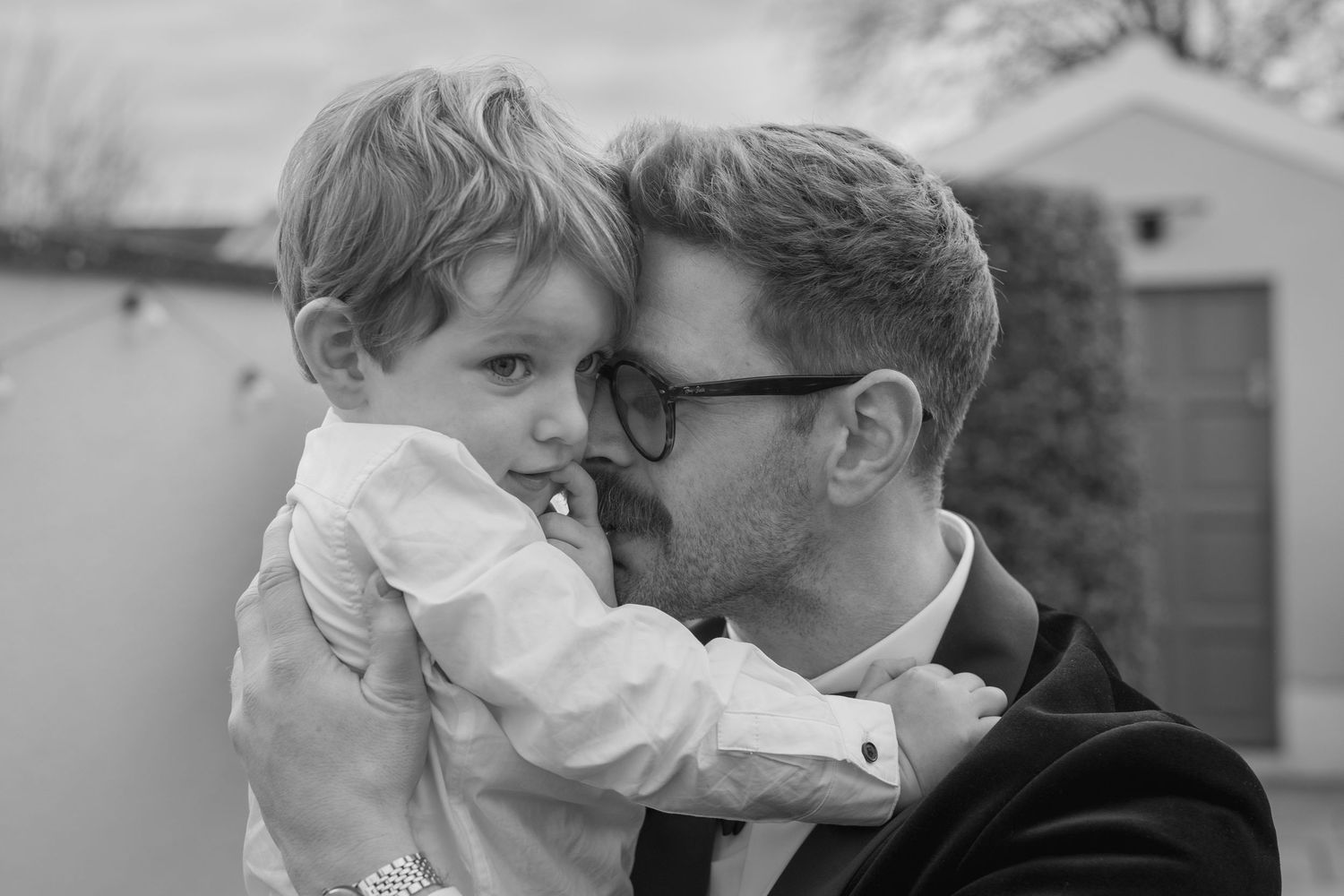 Tender black and white portrait of a groom in suit sharing a quiet moment with a young child.