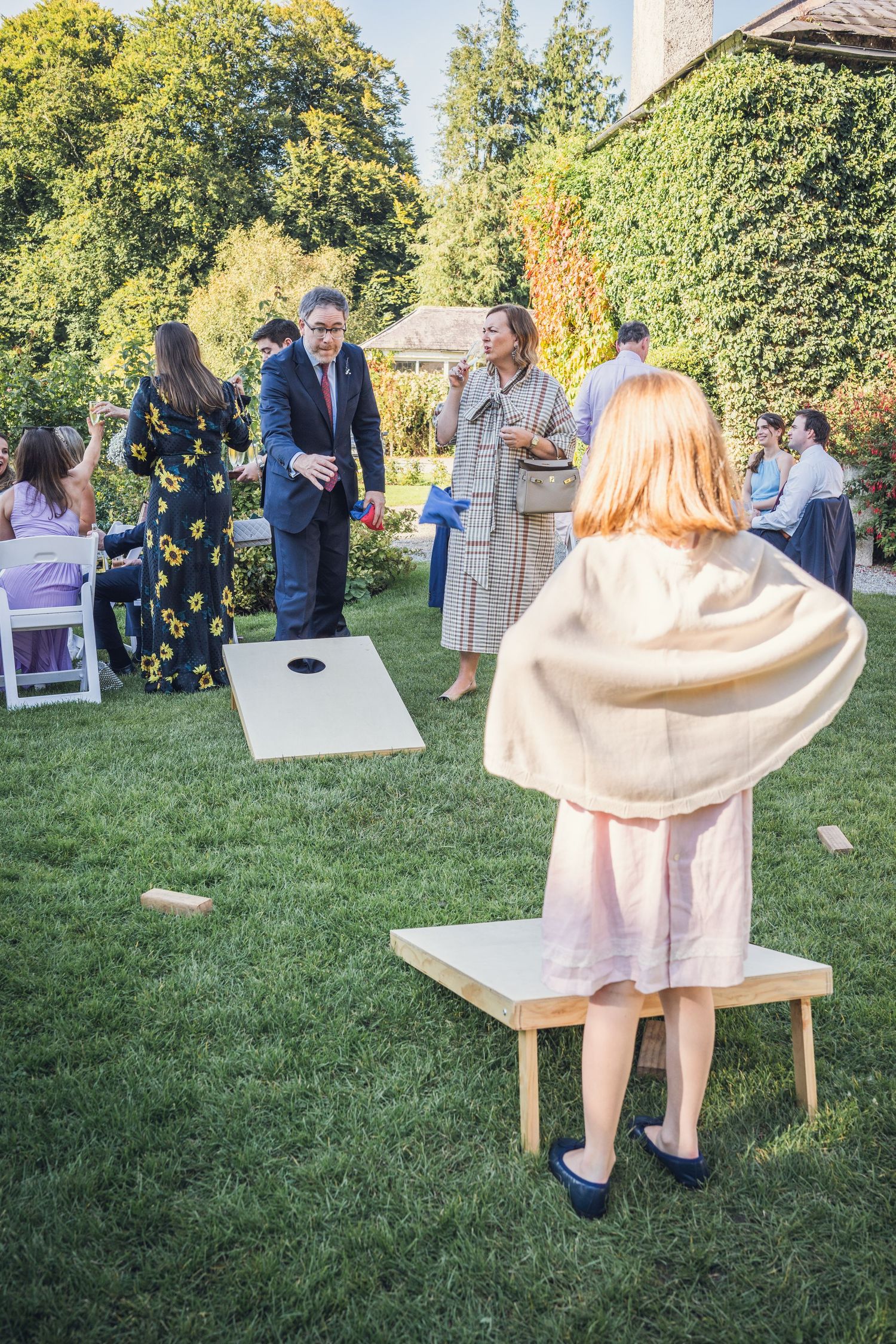 Young girl in pink dress plays cornhole lawn game at elegant outdoor wedding reception.