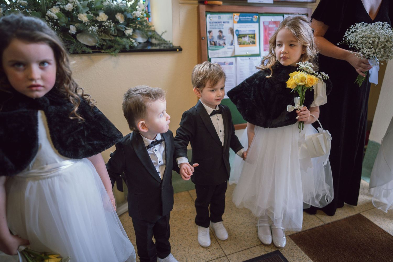 Young flower girls and ring bearers in formal attire prepare to walk down the aisle at a wedding.