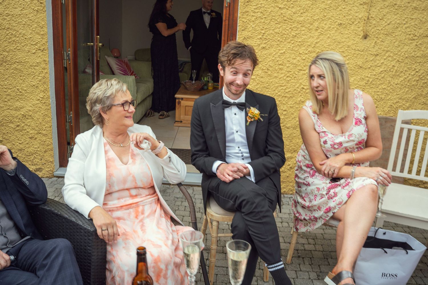 Groom in tuxedo chatting and laughing with guests seated outdoors at wedding reception at outdoor garden wedding reception in Co Meath.