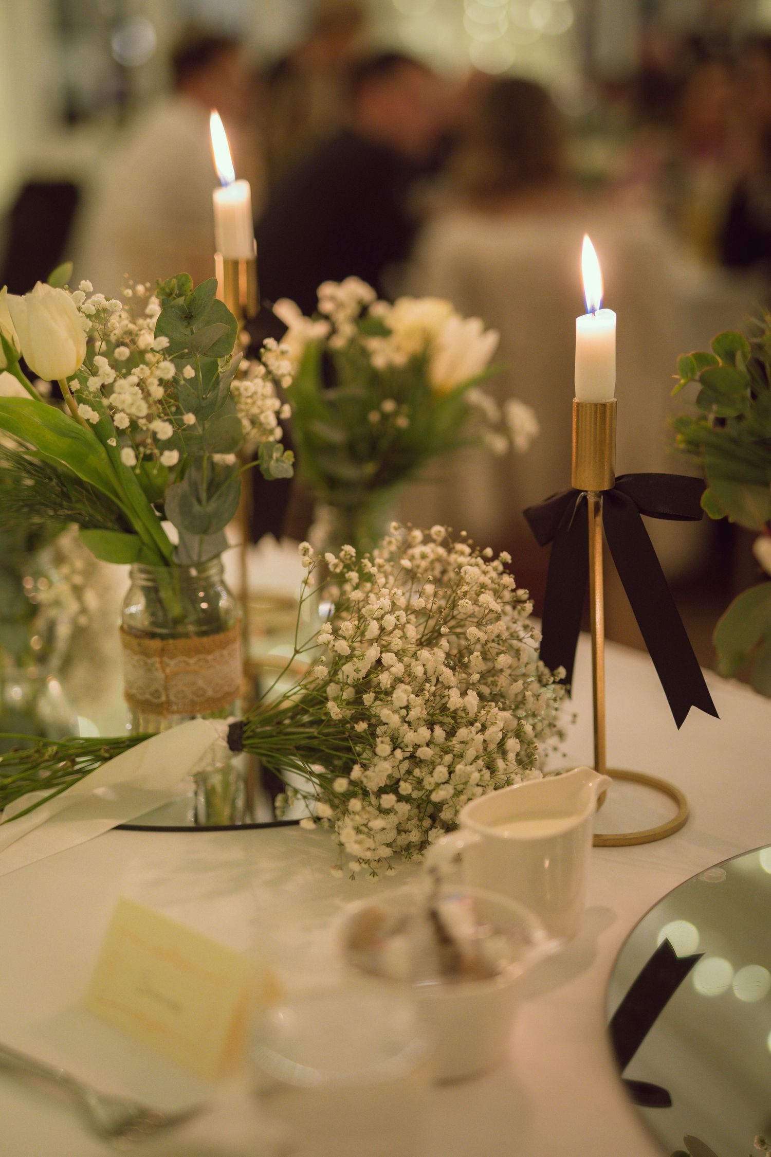 Elegant wedding table centerpiece with gold candlesticks, white candles, baby's breath and roses.