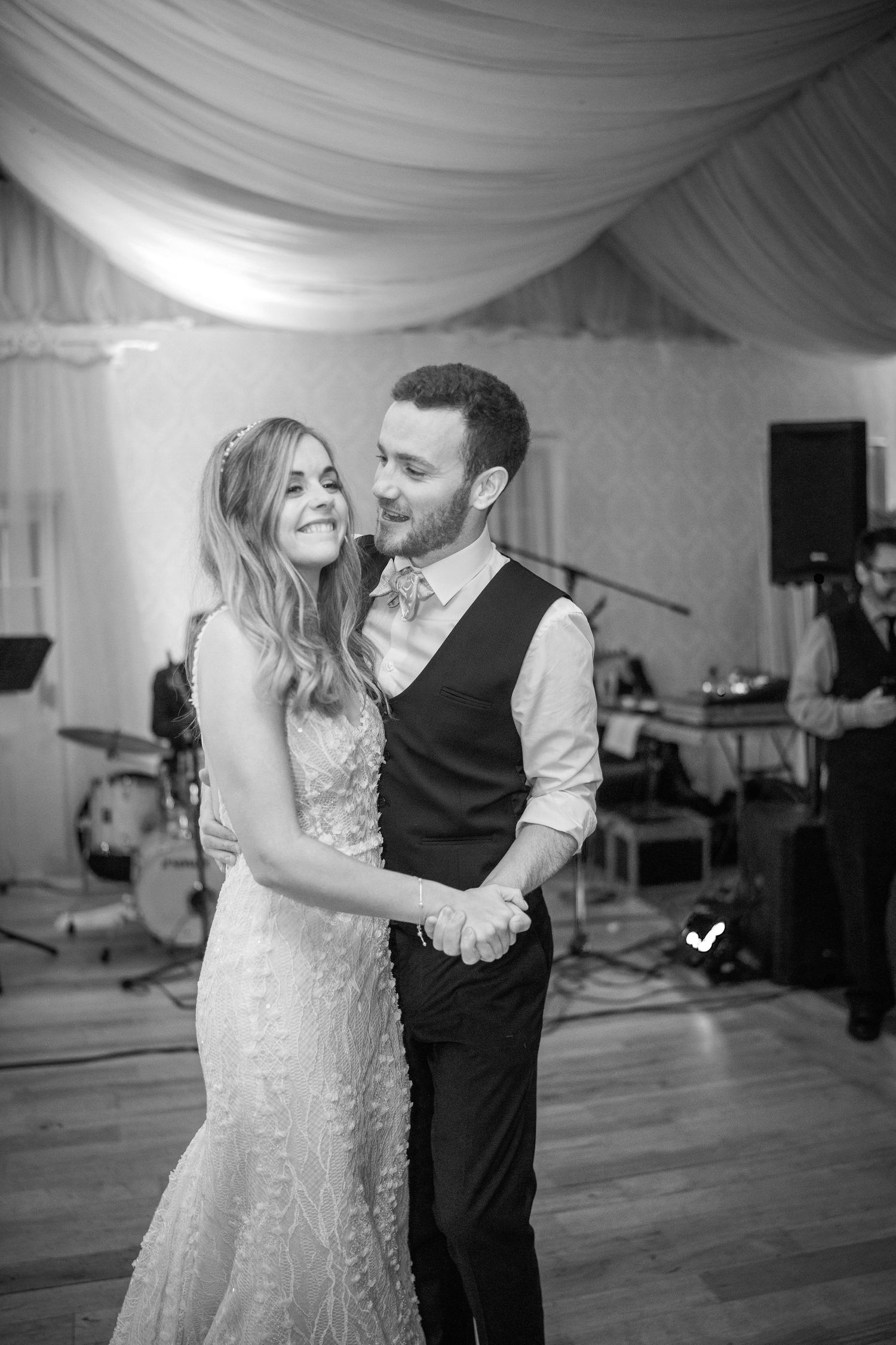 Black and white photo of a bride and groom sharing their first dance with a live band performing behind them.