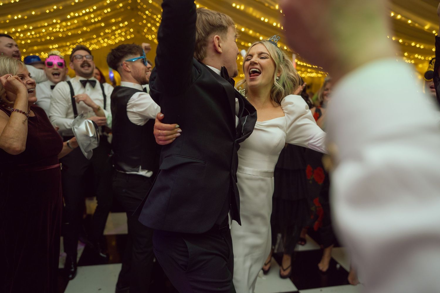 A bride and groom laugh and dance together on the dance floor at their wedding reception.