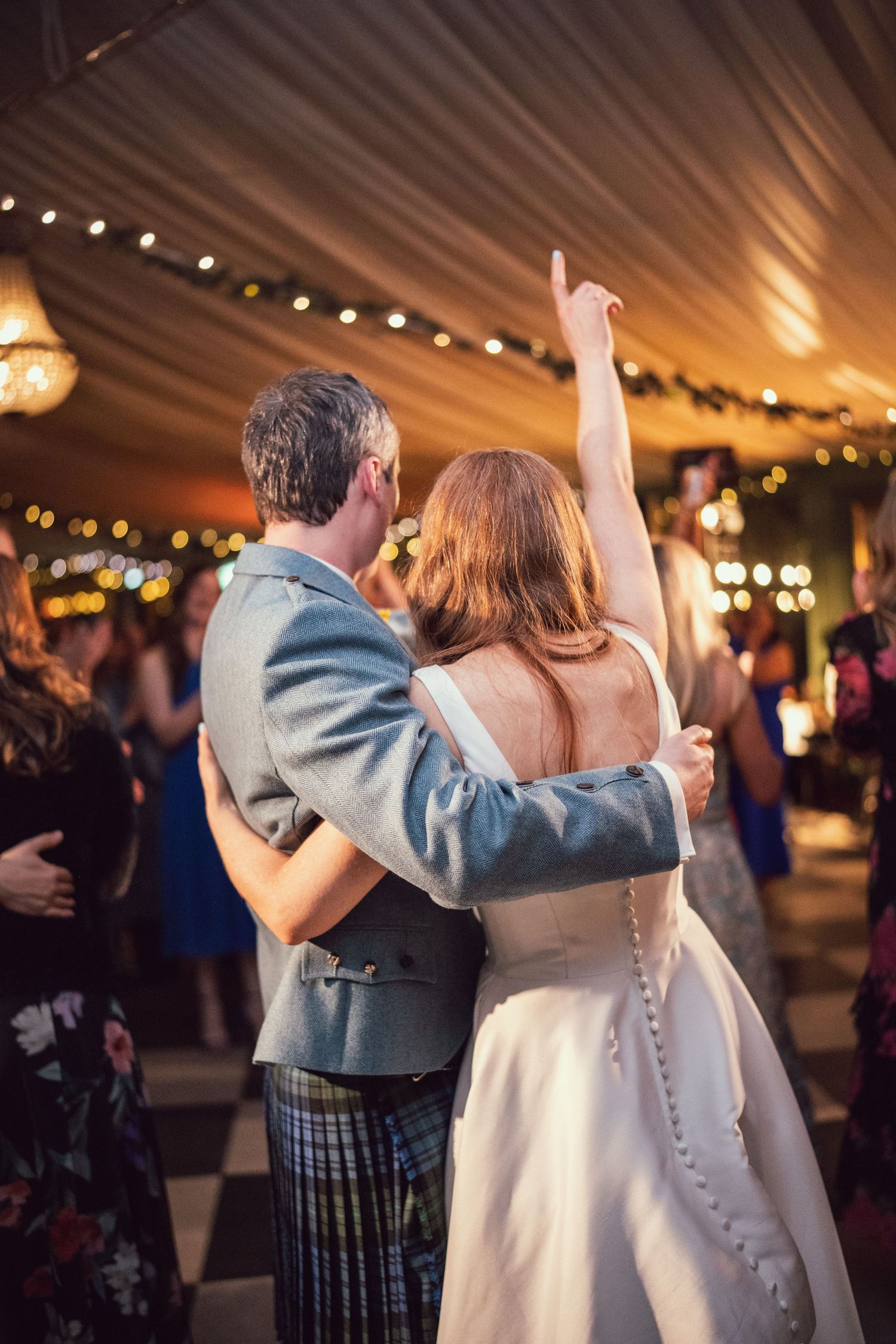 Bride and groom sharing their first dance in a marquee decorated with fairy lights and garlands at their wedding.