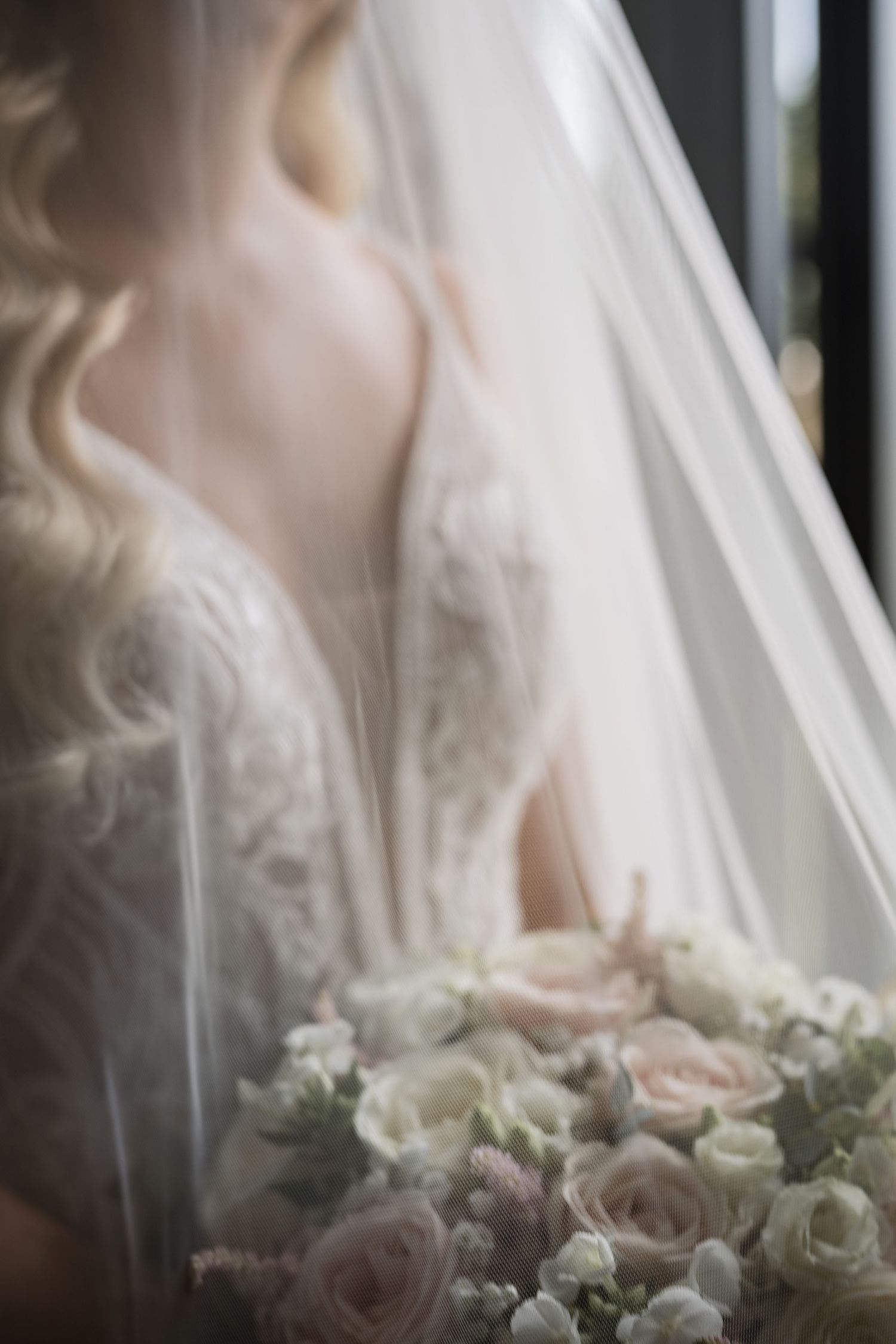 Ethereal bridal portrait showing bride in lace gown holding soft pink and white floral bouquet.