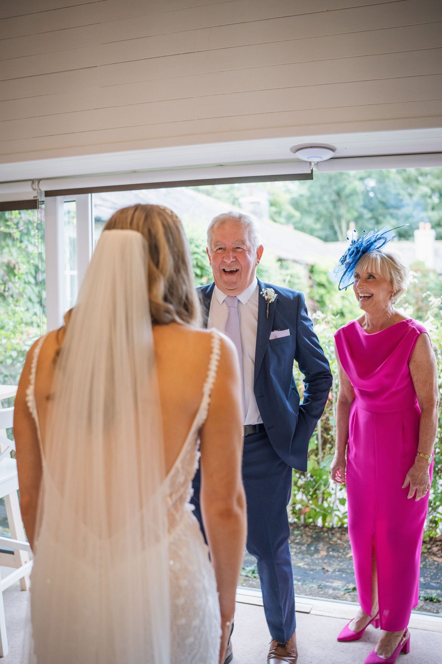 Bride in lace gown sharing a joyful first look moment with her laughing parents.