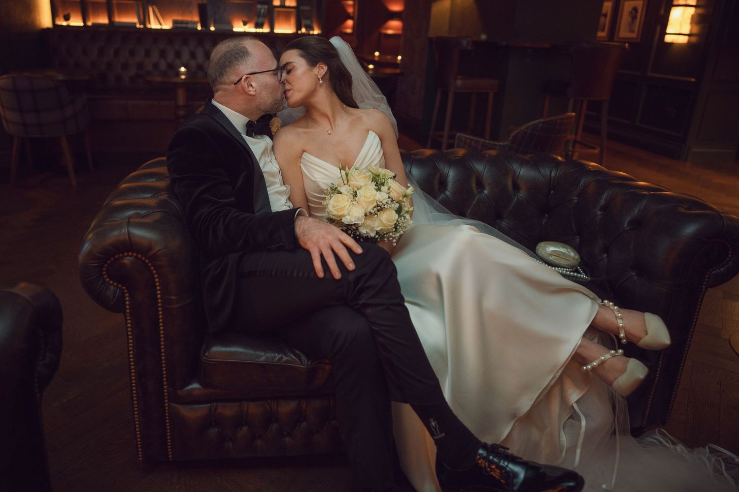 Bride and groom share a kiss on a leather Chesterfield sofa at the Manor House Mount Juliet wedding Kilkenny.