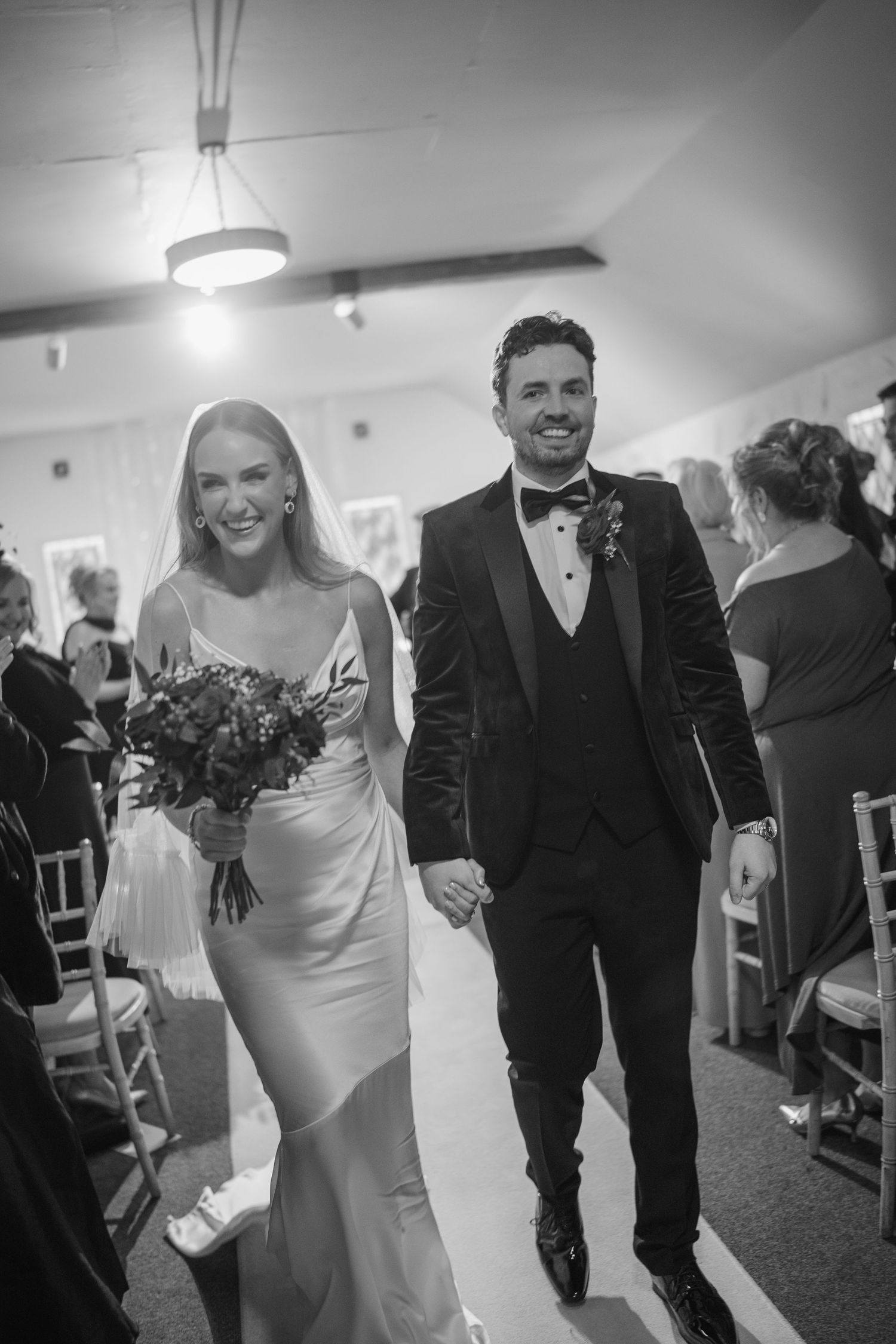 Black and white photo of beaming newlyweds walking hand in hand down the wedding aisle at Rathsallagh House wedding in Wicklow.
