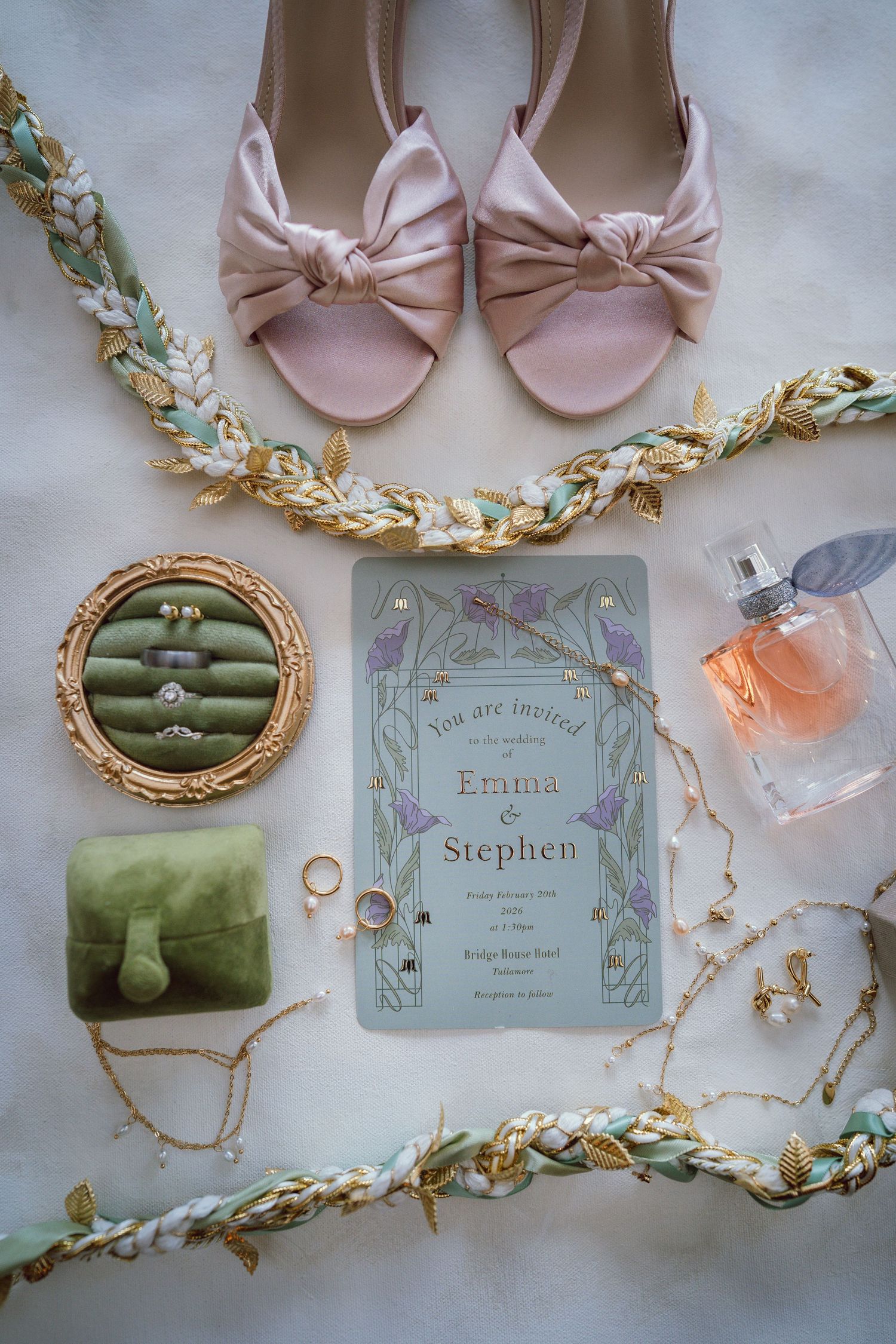 Flat lay of wedding details for Emma and Stephen including pink heels, rings, bouquet, perfume, and floral invitation.