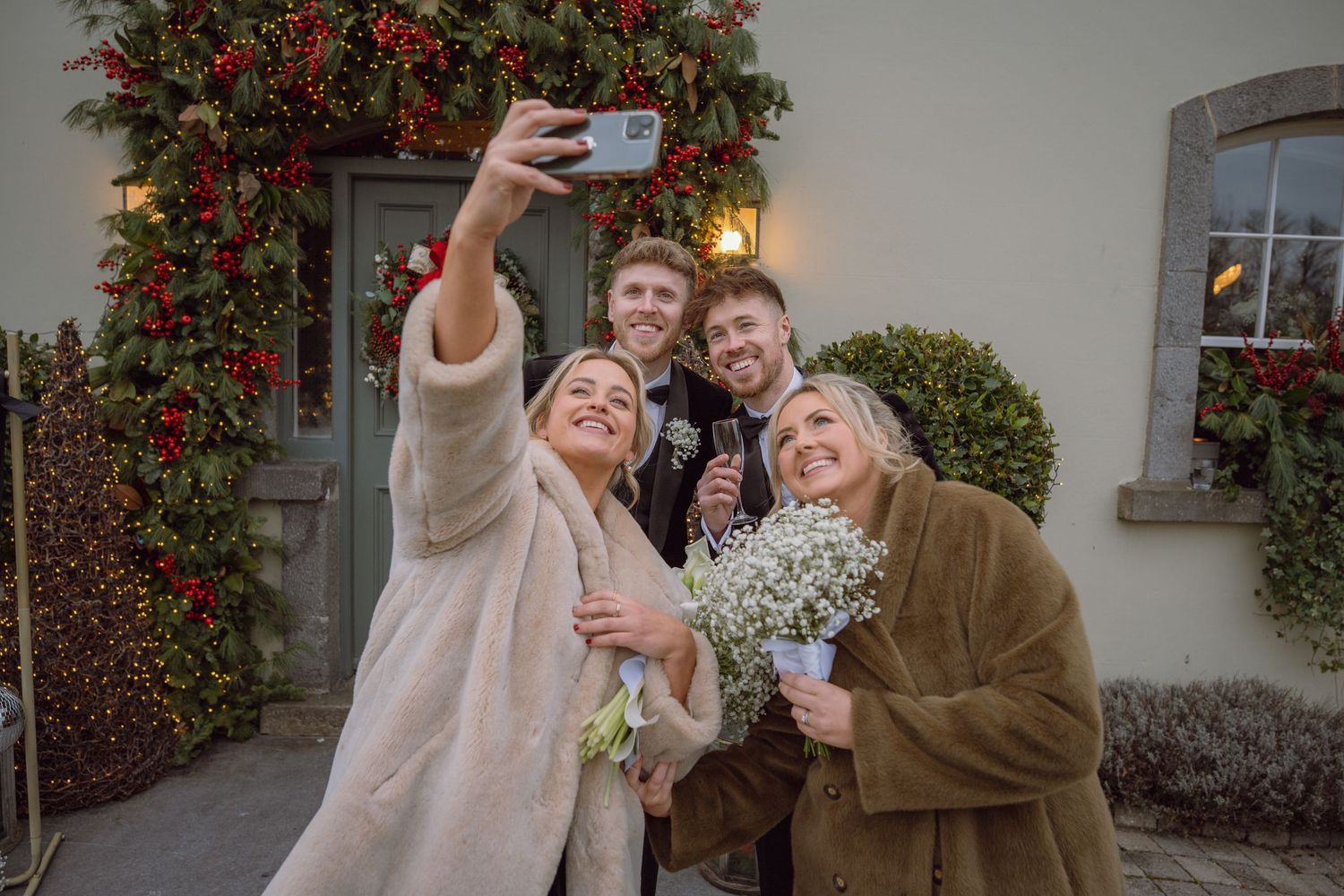 Wedding group takes a fun selfie outside a festively decorated venue entrance.