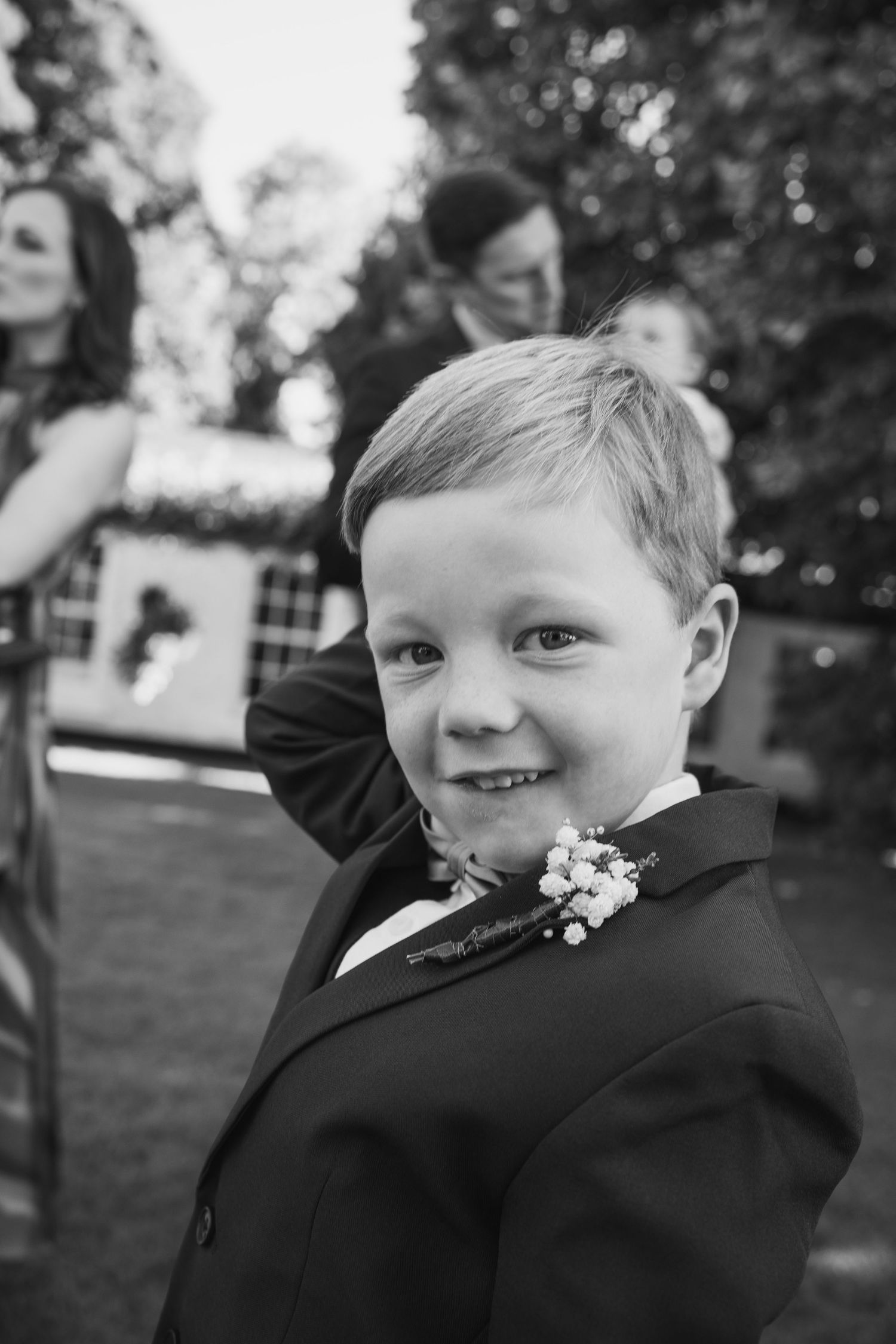 Black and white portrait of smiling boy in suit with boutonniere at wedding.