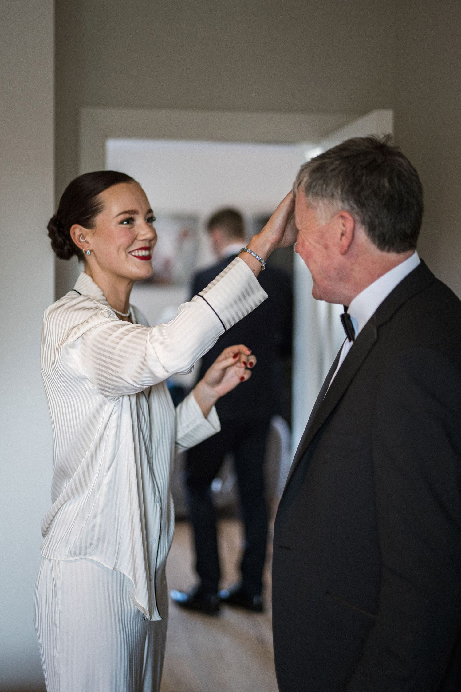 Smiling bride in striped robe adjusting older gentleman's hair while getting ready before the wedding ceremony.
