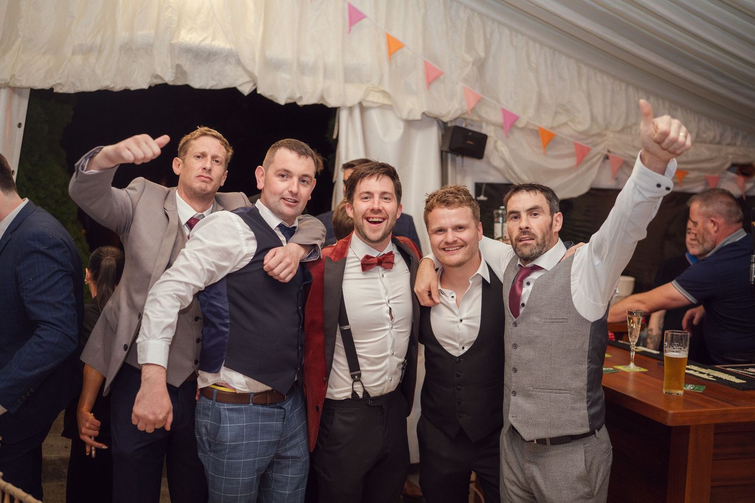 Five groomsmen celebrating and posing together in a decorated wedding marquee at goutdoor garden wedding reception in Co Meath.
