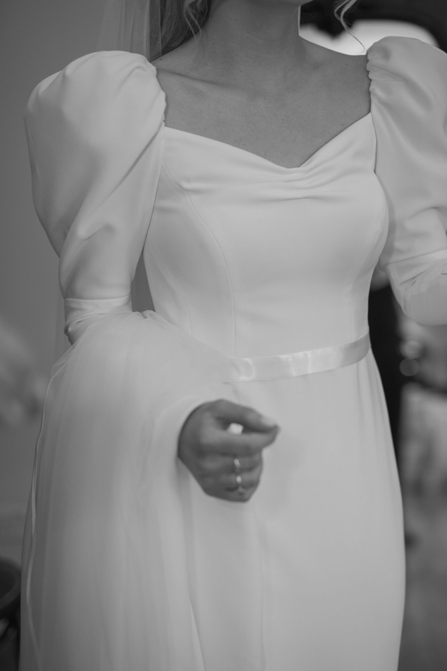 Close-up black and white detail of bride's white gown with puff sleeves and satin belt.