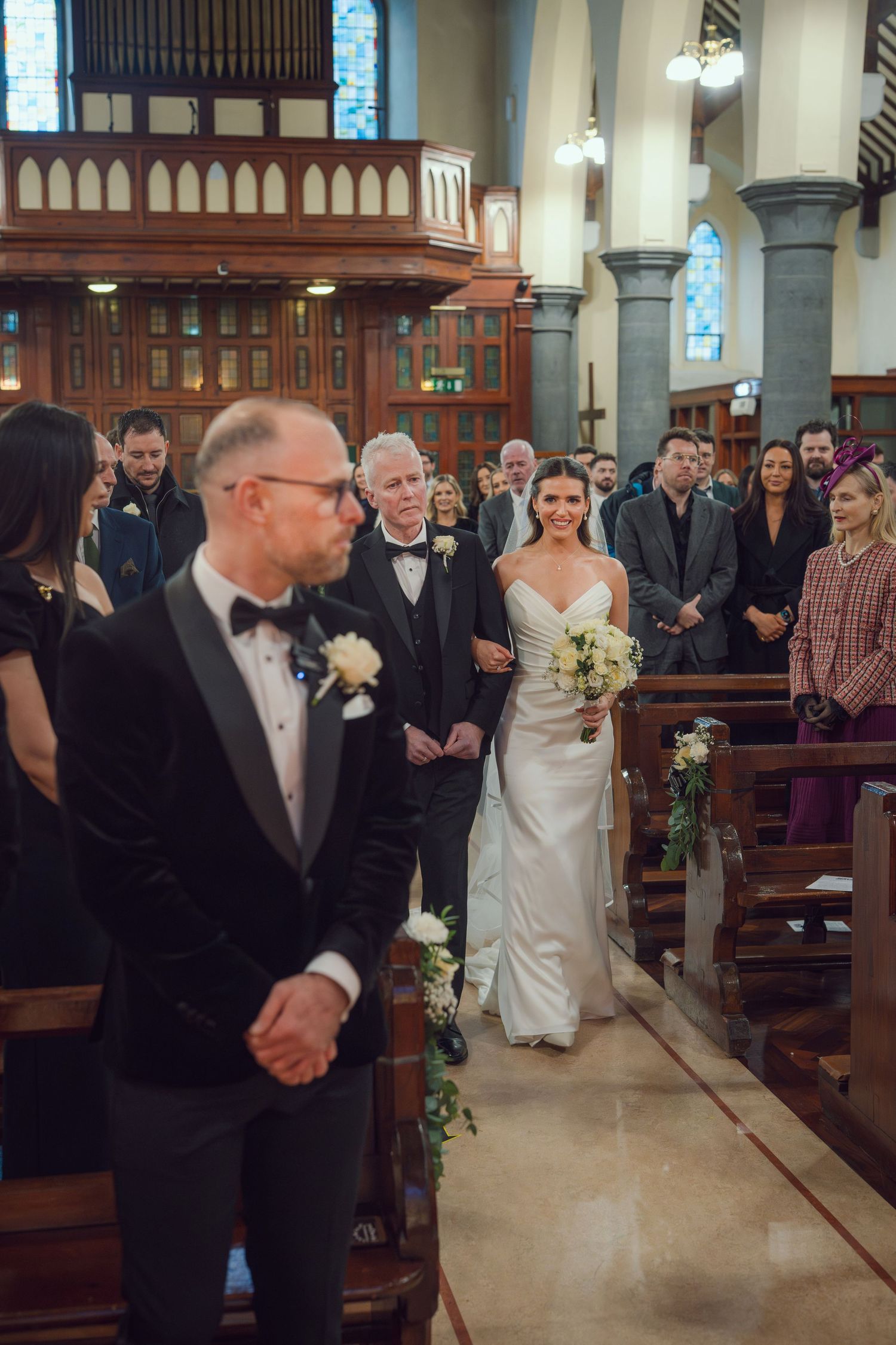 Bride walking down church aisle with bouquet as groom waits at altar during wedding ceremony at Mount Juliet wedding Kilkenny.