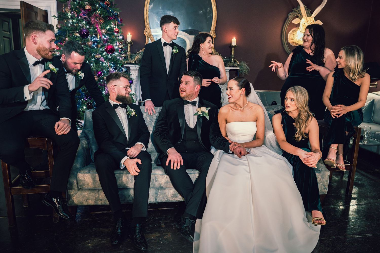 Wedding party laughing and celebrating together near a Christmas tree in a warmly lit elegant venue.