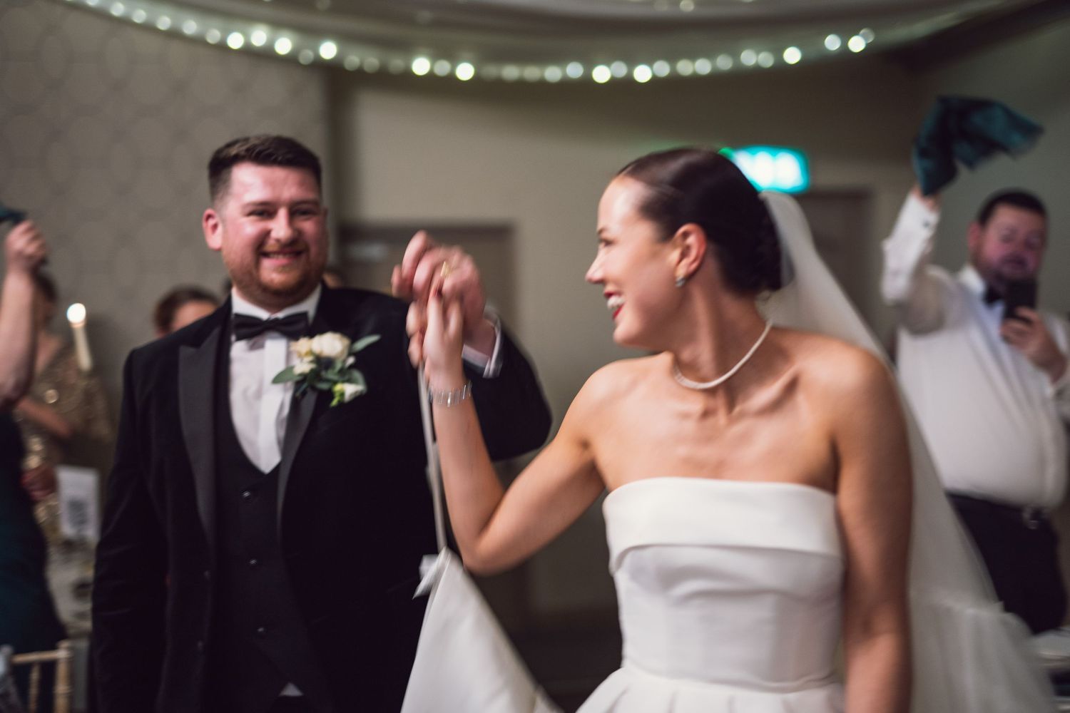 Bride and groom sharing a joyful moment on the dance floor, bride in strapless white dress with pearl necklace.