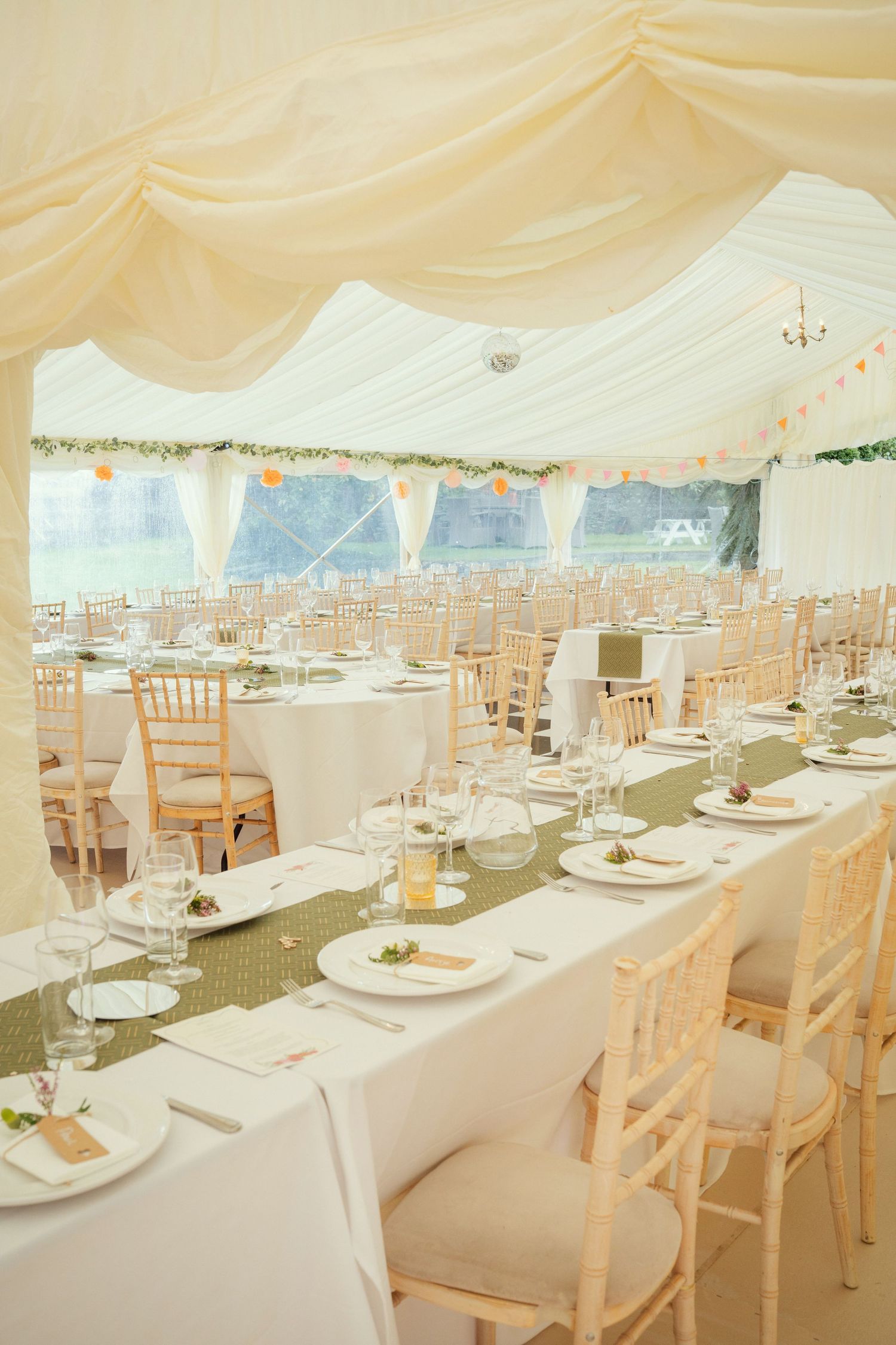 Elegant wedding marquee with white draping, round tables, and chiavari chairs set for a reception.