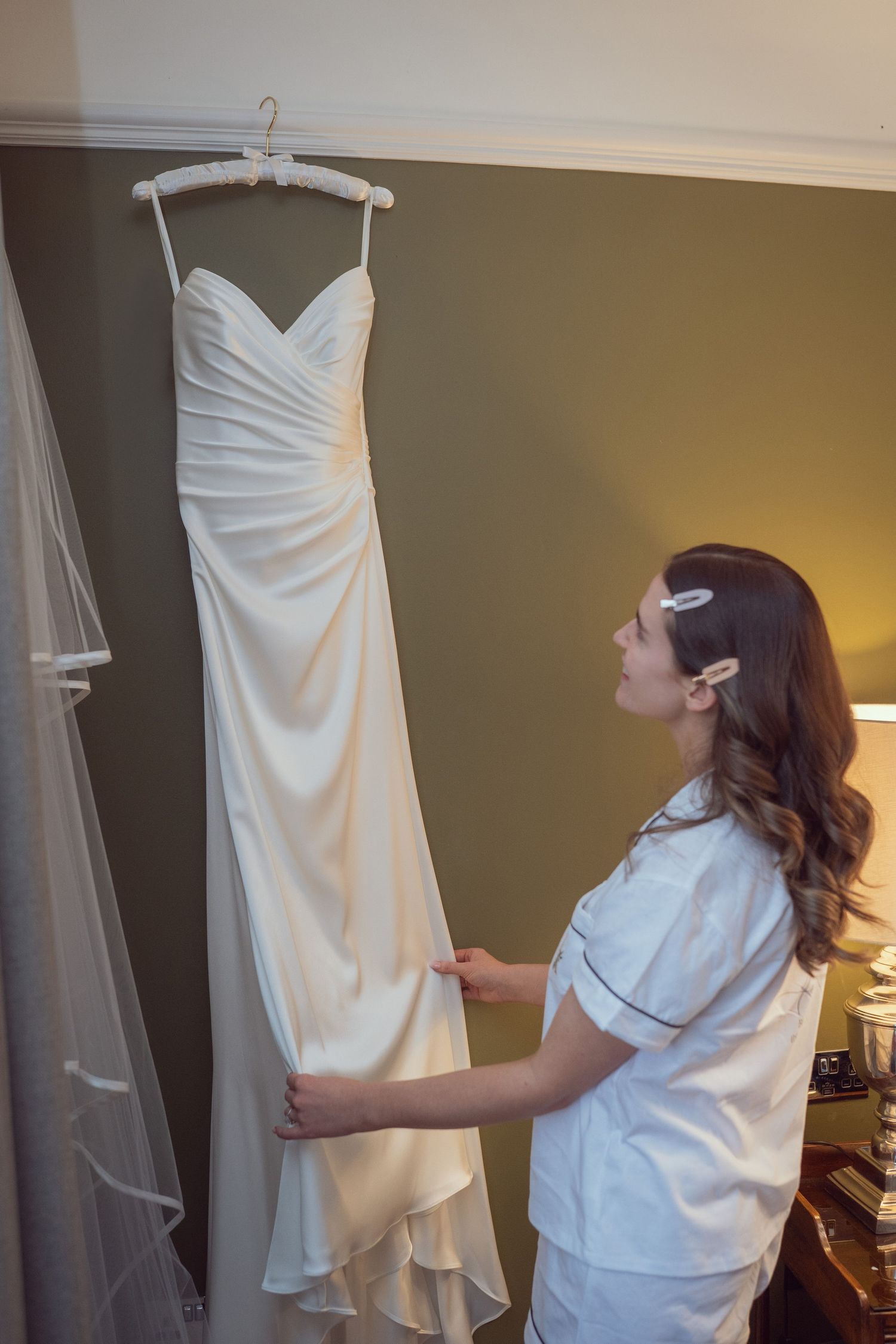 Bride in pajamas admiring her hanging elegant strapless wedding dress at the Manor House Mount Juliet wedding Kilkenny.