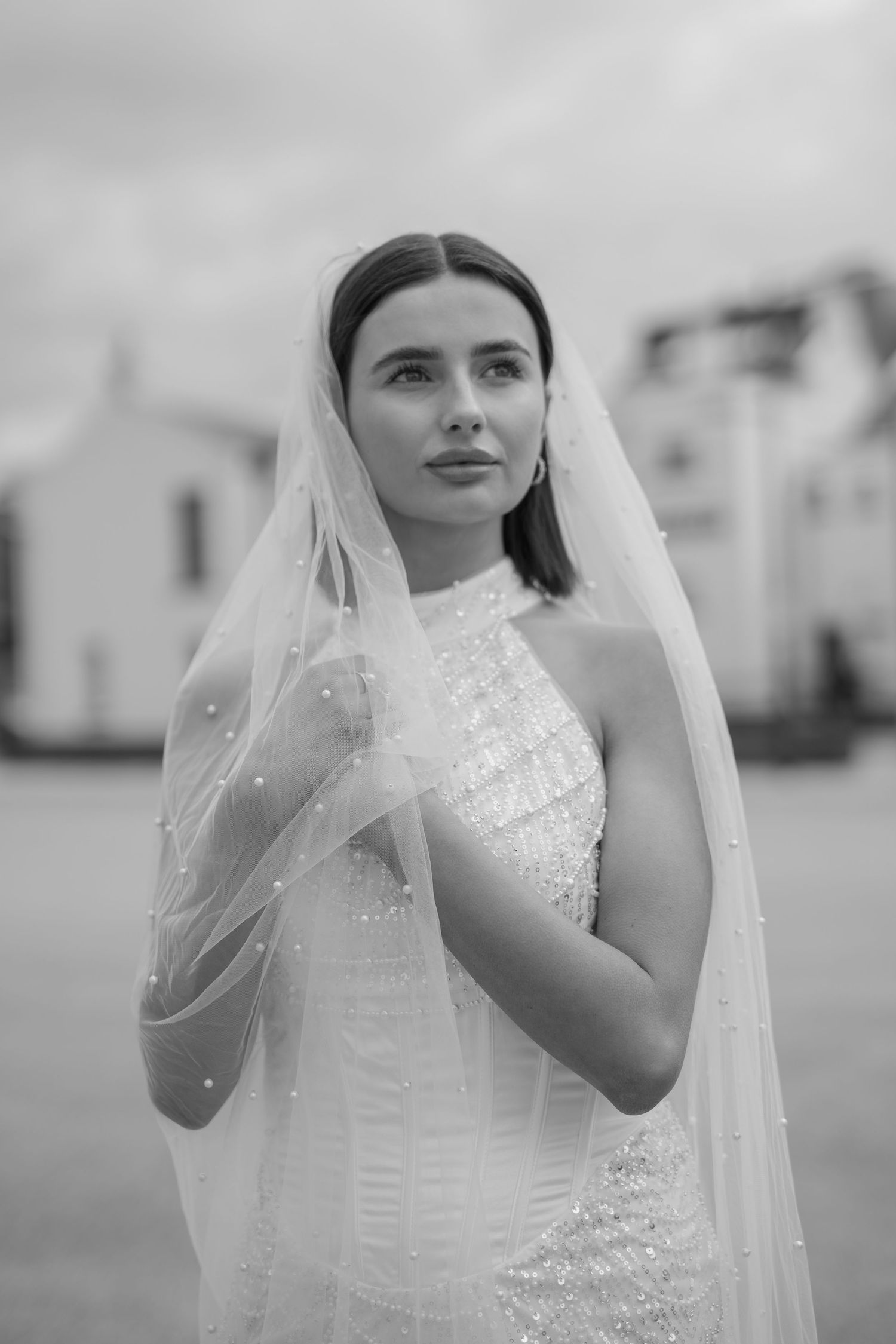 Beautiful bride wearing pearl-dotted veil and beaded halter gown in classic black and white portrait.