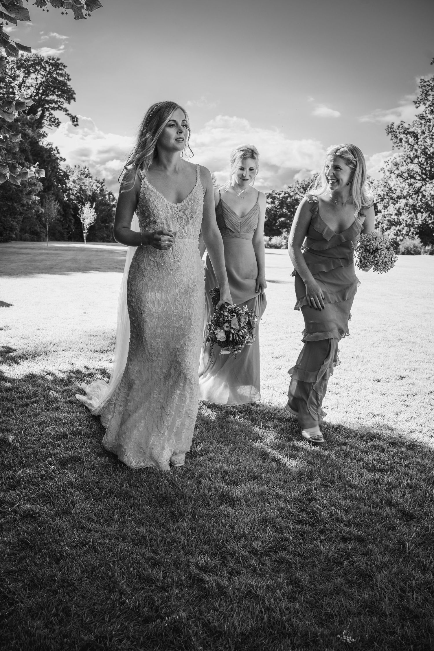 Bride in beaded gown walks with two bridesmaids across sunlit lawn at Rathsallagh House wedding in Wicklow.