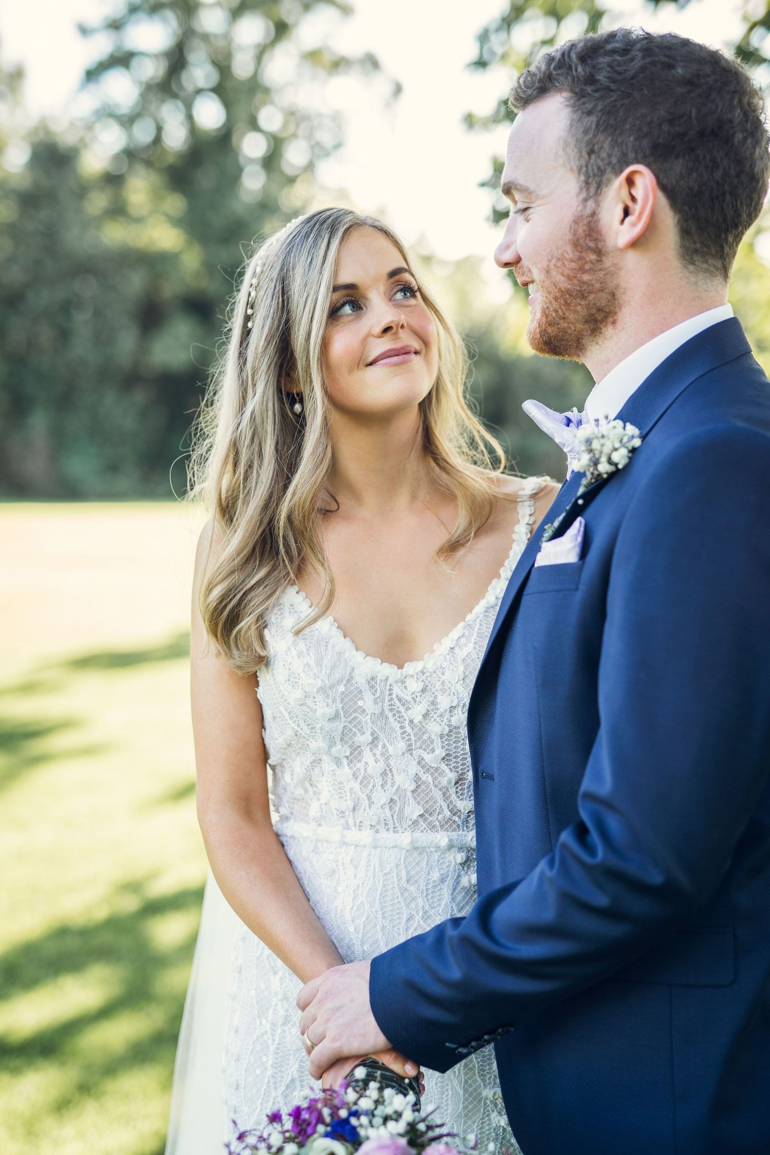 Bride gazing lovingly at red-bearded groom in navy suit at garden wedding.