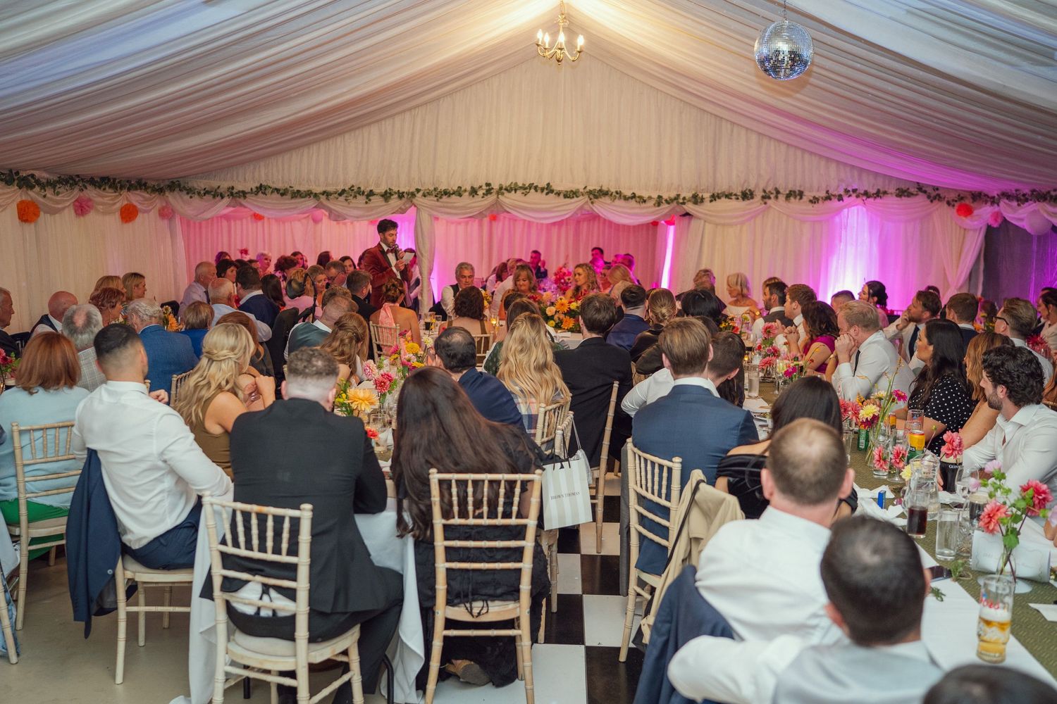 A large wedding reception with guests seated at decorated tables inside a bright marquee at outdoor garden wedding reception in Co Meath.