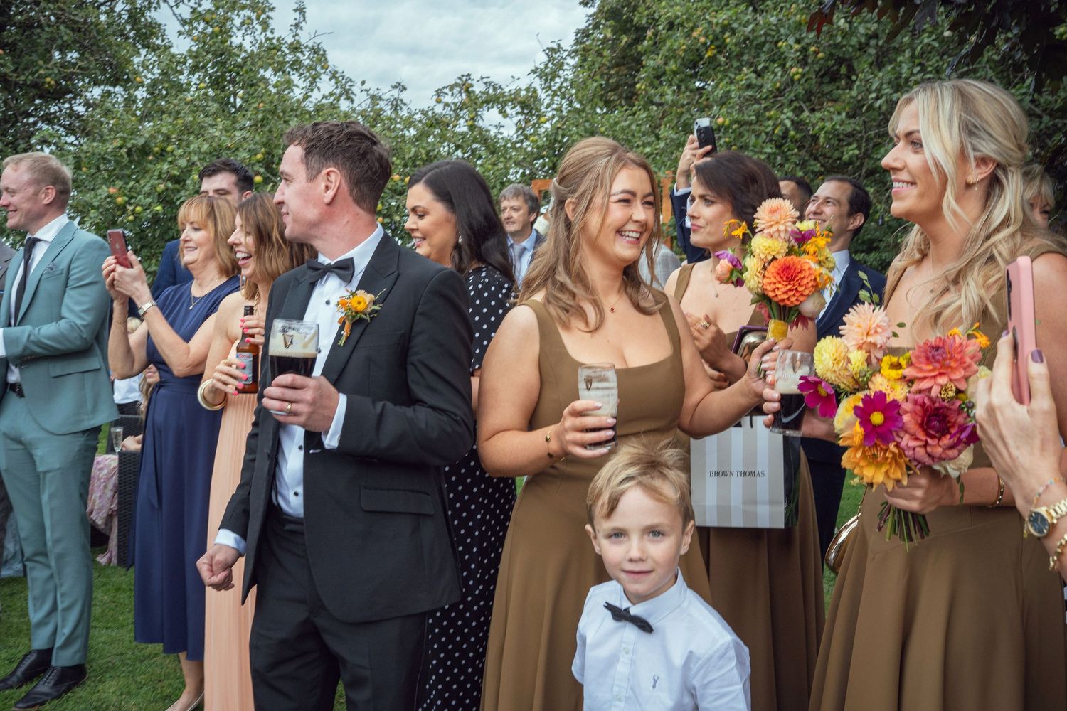 Smiling wedding guests in elegant attire holding drinks and colorful bouquets at outdoor garden wedding reception in Co Meath.