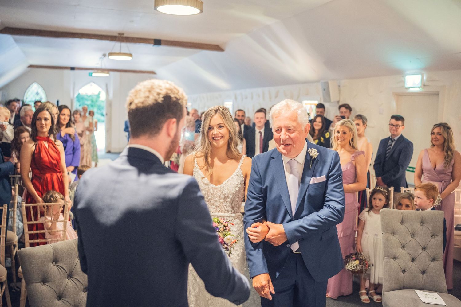 Father of bride shakes grooms hand during indoor wedding ceremony.