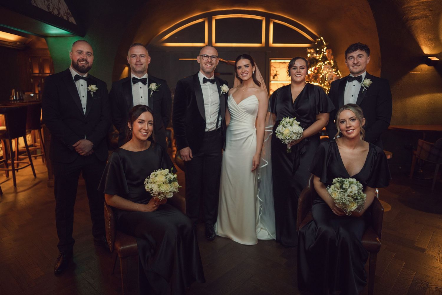 Wedding party group portrait in a warmly lit venue with bride and groom centered at the Manor House Mount Juliet wedding Kilkenny.